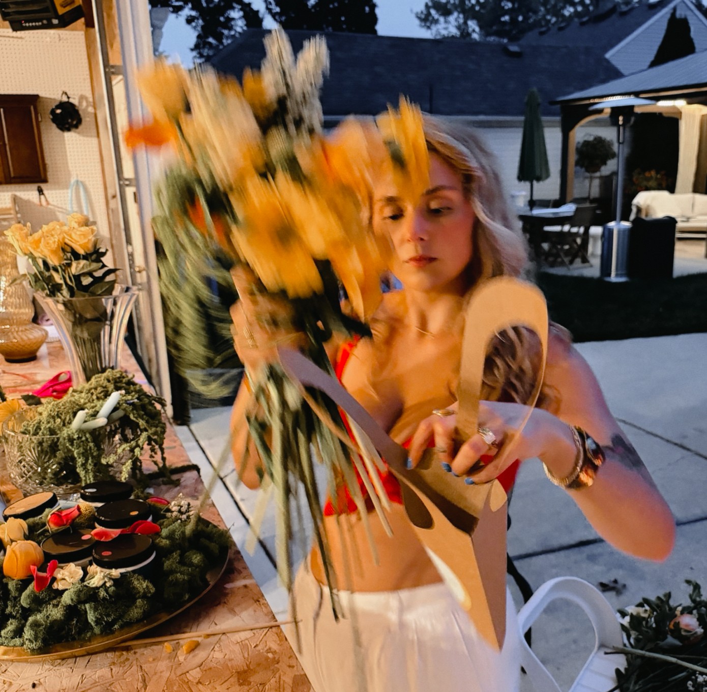 Young woman with blonde hair opening a large bouquet of yellow flowers indoors, with a table of decorated cupcakes nearby.