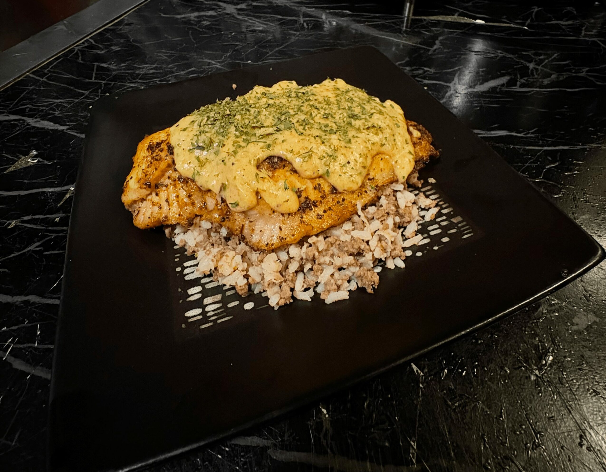 Cooked chicken topped with green herb sauce, served on a bed of rice on a black plate.