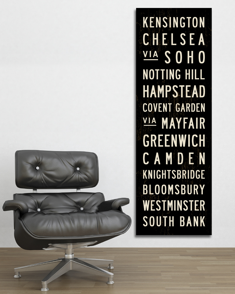 Black vertical sign with white text listing London locations, next to a black leather office chair on a wooden floor.