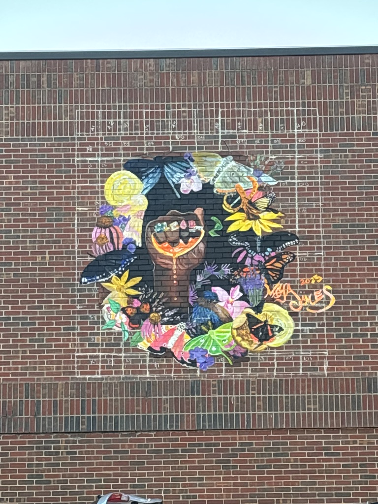 Colorful mural of a smiling woman with flowers and animals on a brick wall.