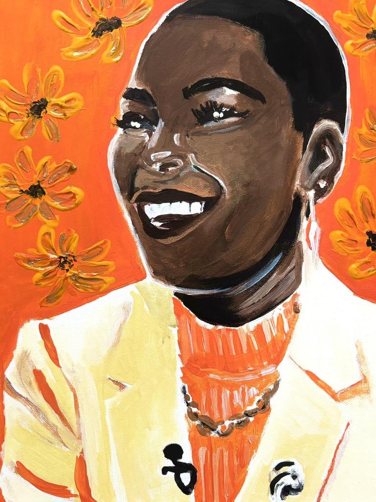 Portrait of a smiling person with short hair, wearing a yellow jacket and orange top, surrounded by orange flowers.
