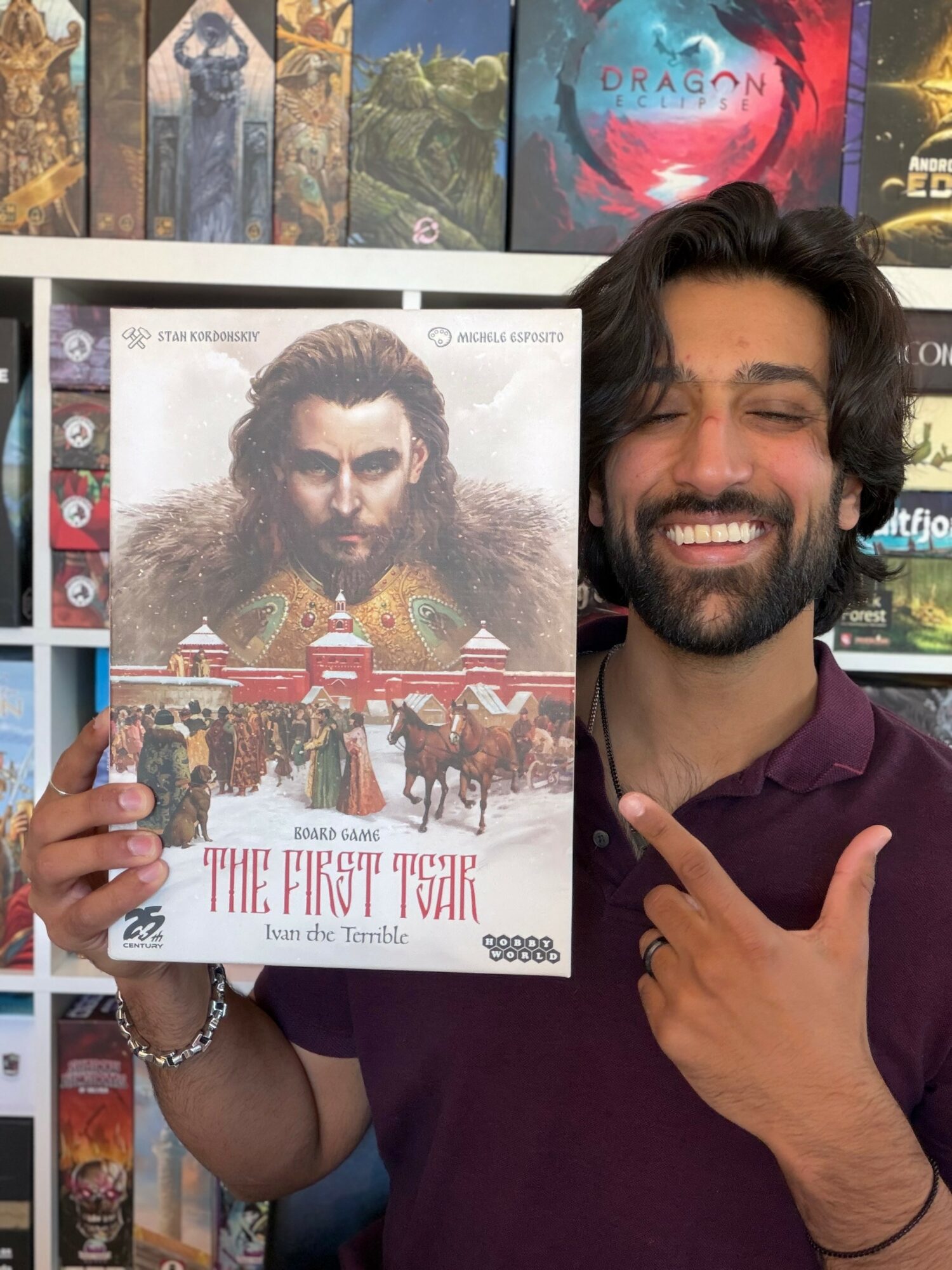 Man with dark hair and beard smiling, holding a book titled 'The First Train' in front of a bookshelf.