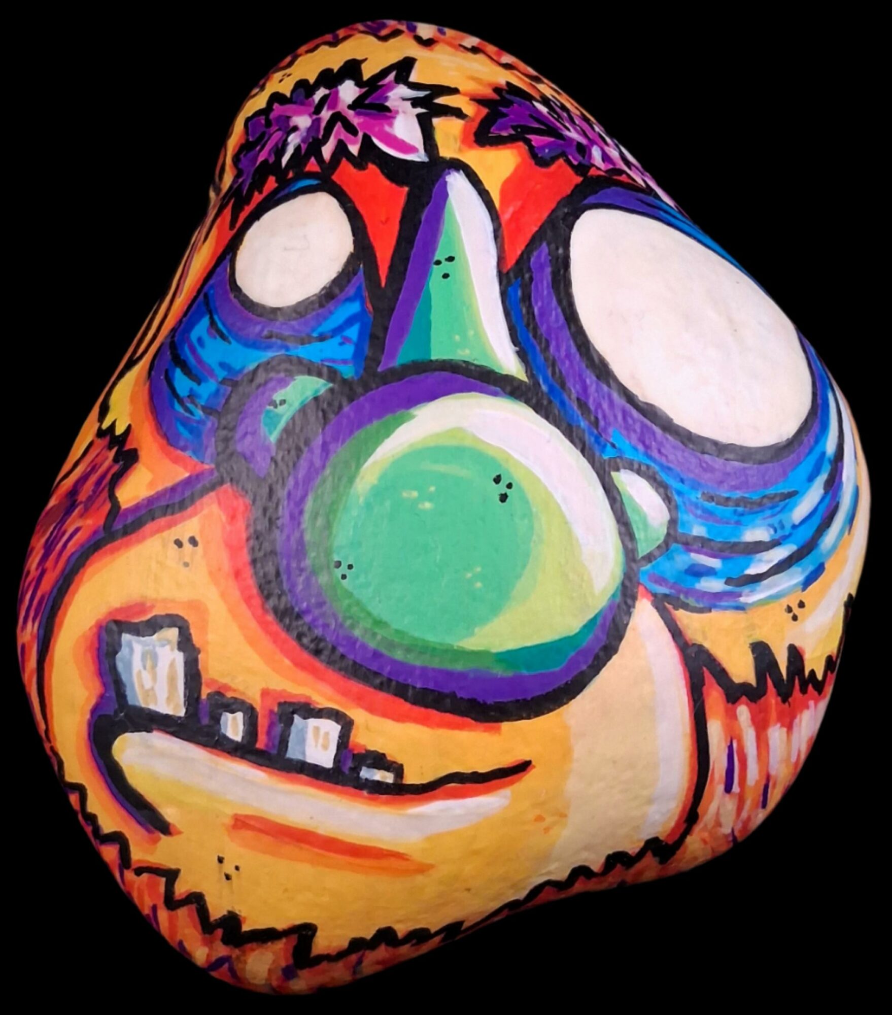 Colorful painted rock with a clown face, large eyes, green nose, and a wide smile, on a black background.