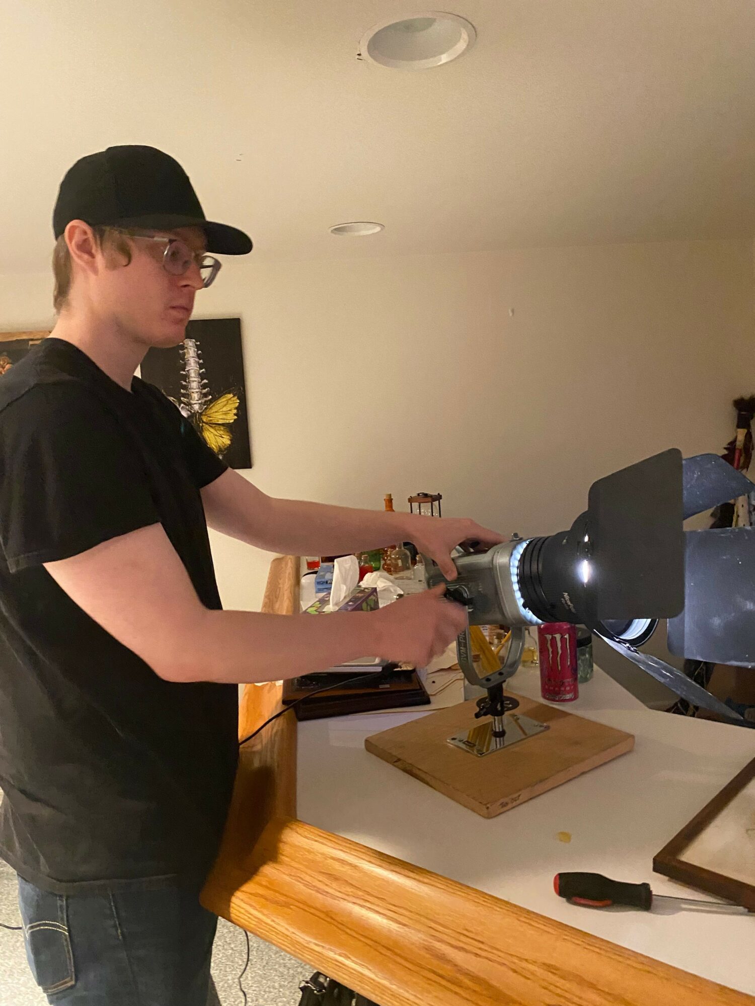 Person using a drill at a workbench in a room with wooden furniture and framed pictures on the wall.