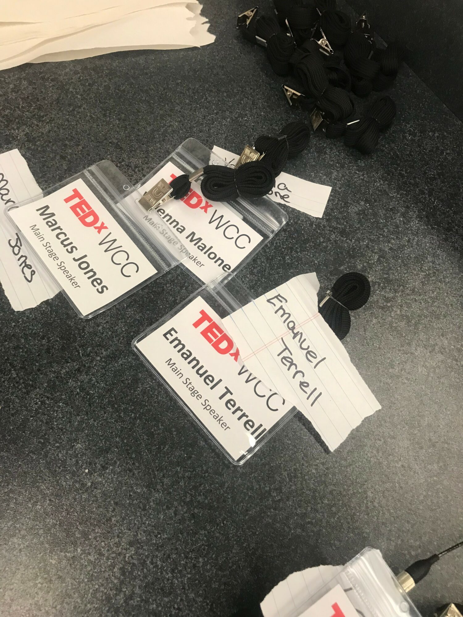 Three TEDx event badges with lanyards and a handwritten note on a gray surface.