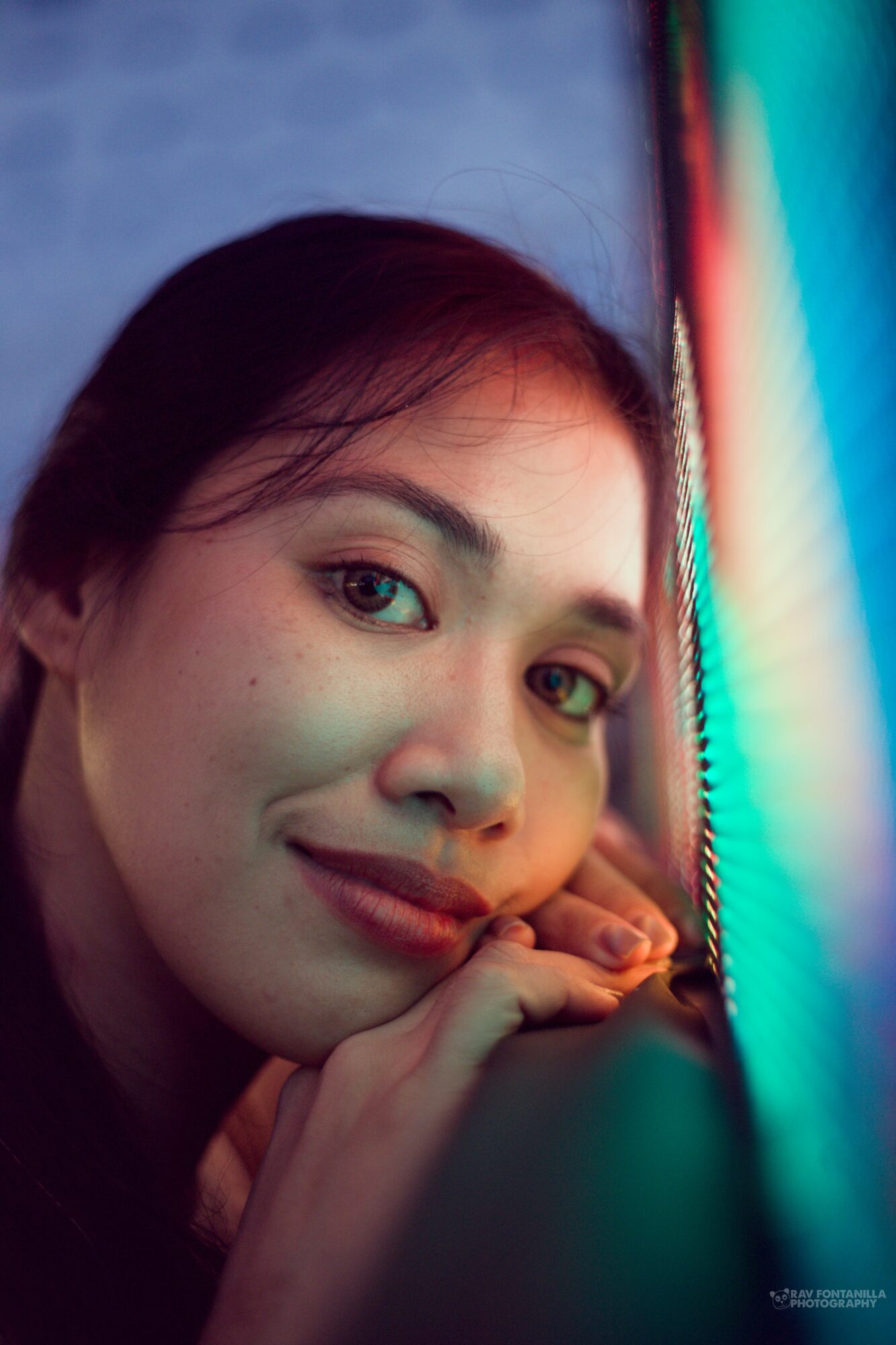 Close-up of a woman with short dark hair, smiling, illuminated by colorful neon lights.