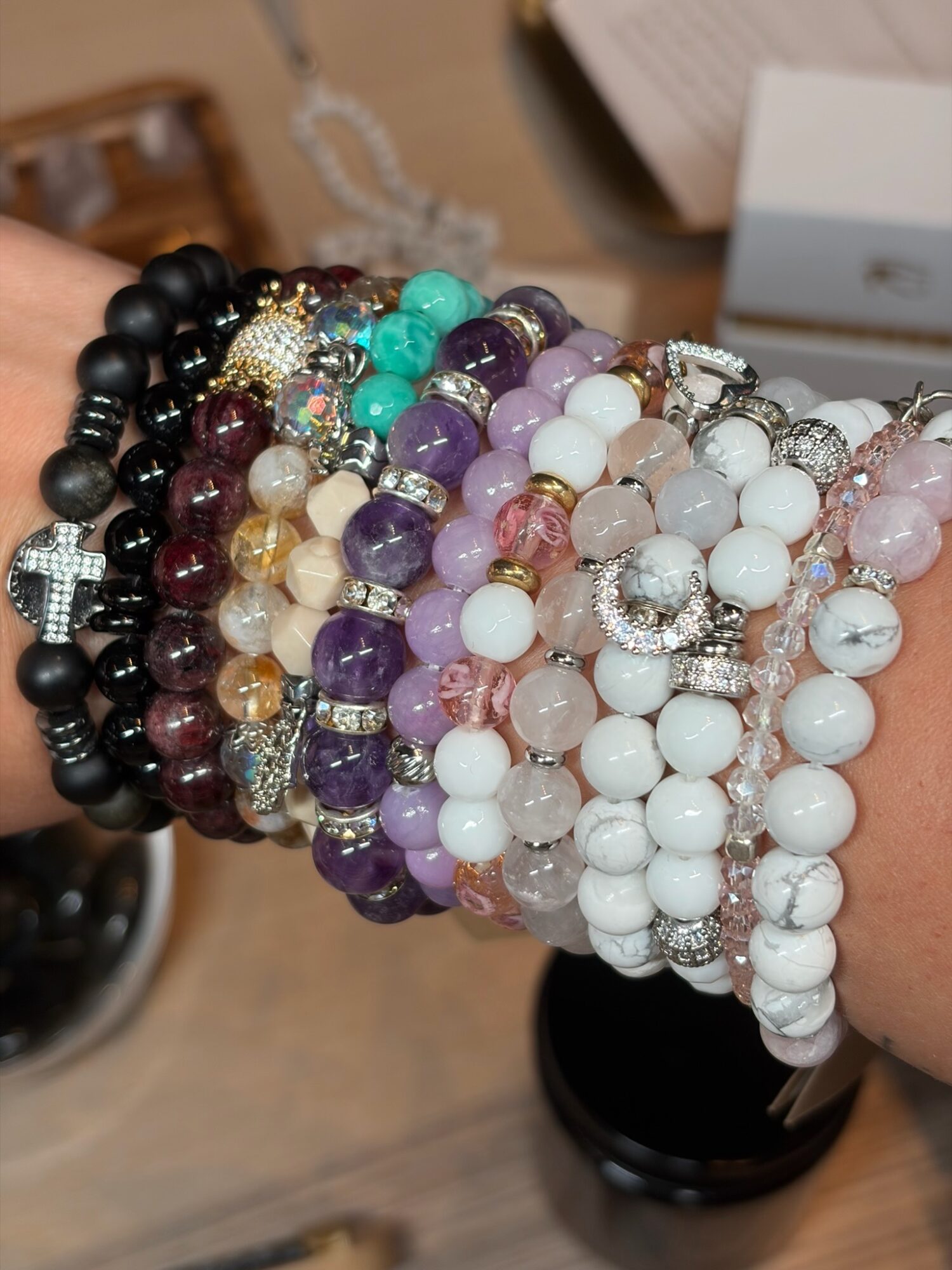 Multiple colorful beaded bracelets stacked on a wrist, with various colors and styles, including black, purple, white, and pink beads.