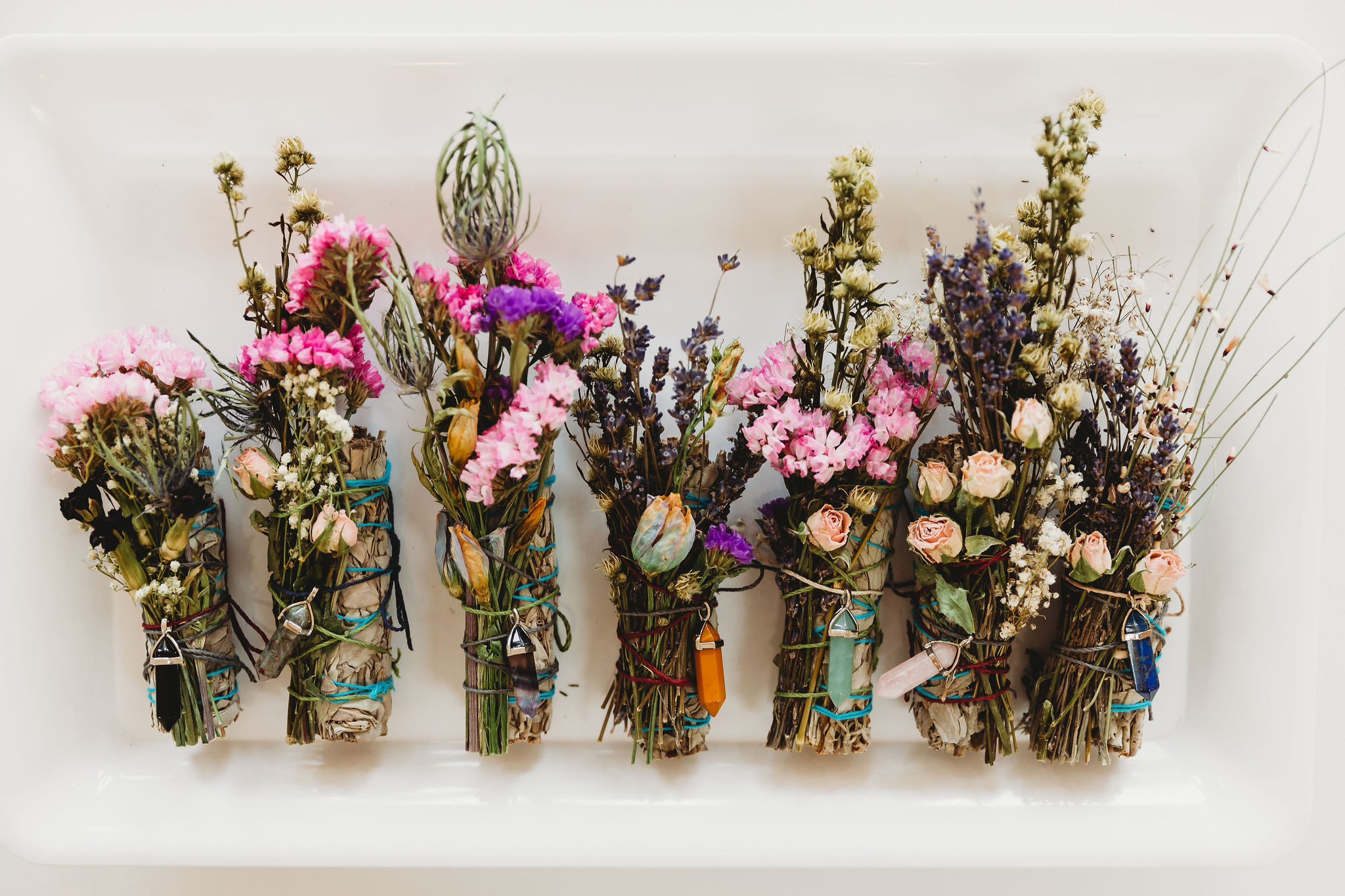 Multiple small bouquets of dried flowers in glass jars on a white surface.