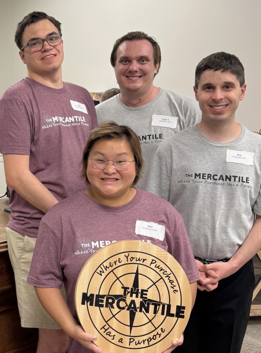 Four people standing together, smiling, with a sign that reads 'The Mercantile' in front of them.