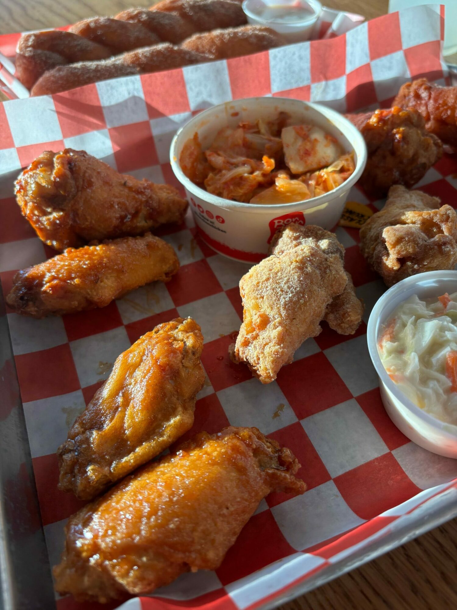 Fried chicken pieces with dipping sauces on a checkered tray, some chicken pieces are breaded and crispy, others are sauced.
