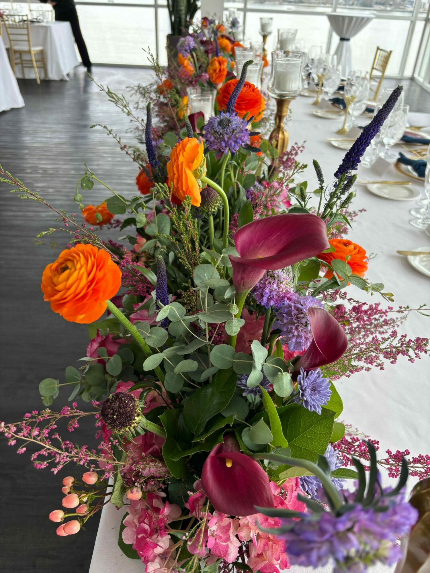 Colorful flower arrangement with purple, pink, orange, and green flowers and foliage on a table.