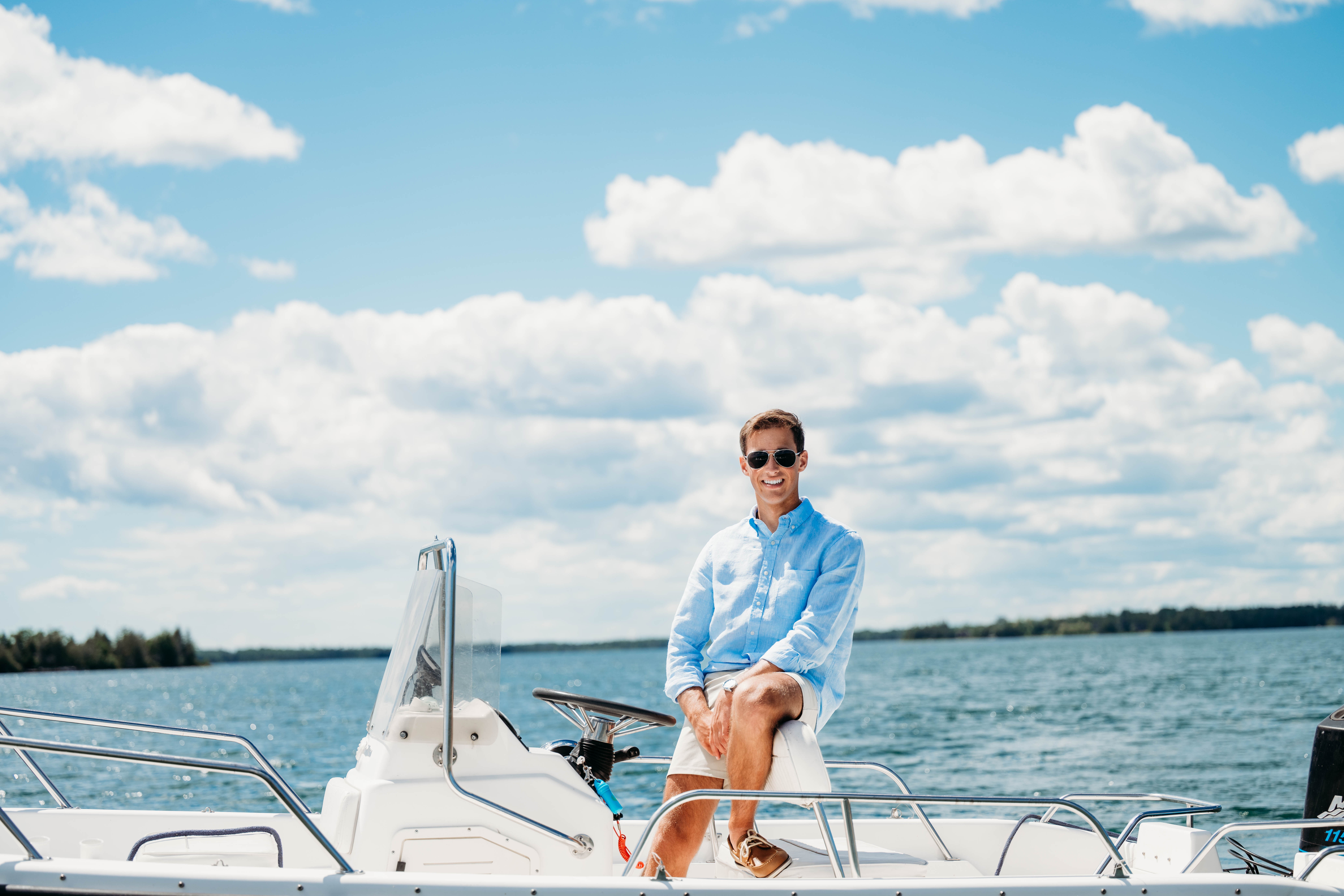 Person sitting on a boat with water and sky in the background, wearing sunglasses and a light blue shirt.