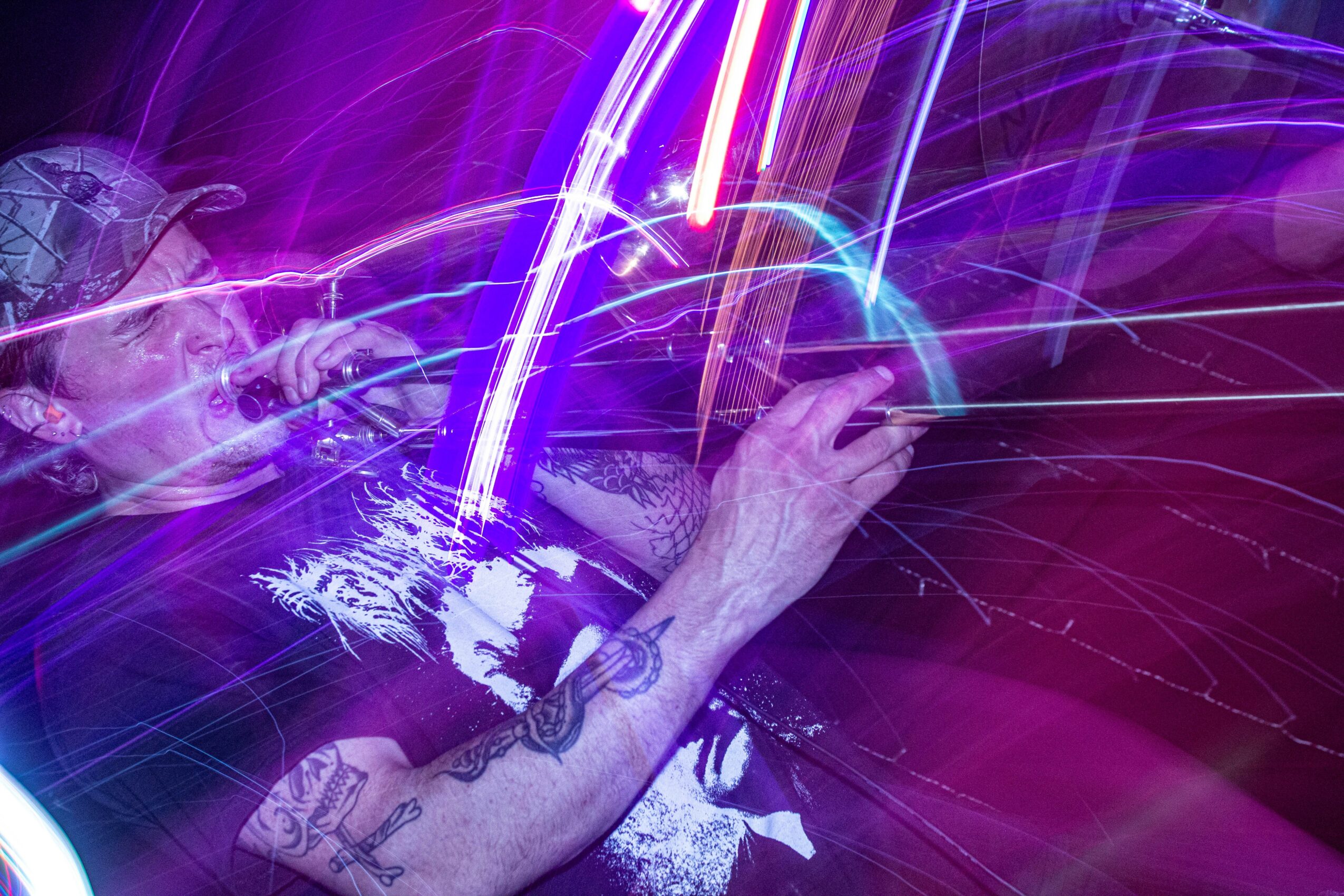 Person with tattoos using DJ equipment with colorful light effects and streaks of light, vibrant purple and blue hues.