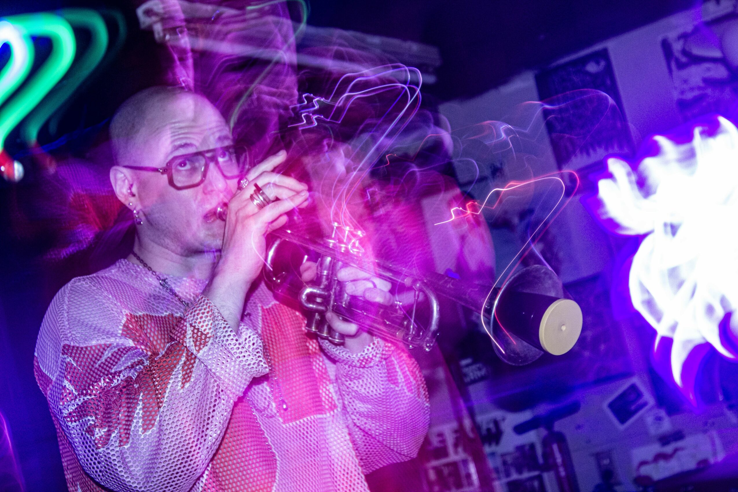 Person with glasses and shaved head smokes in a colorful, neon-lit environment with abstract light patterns.