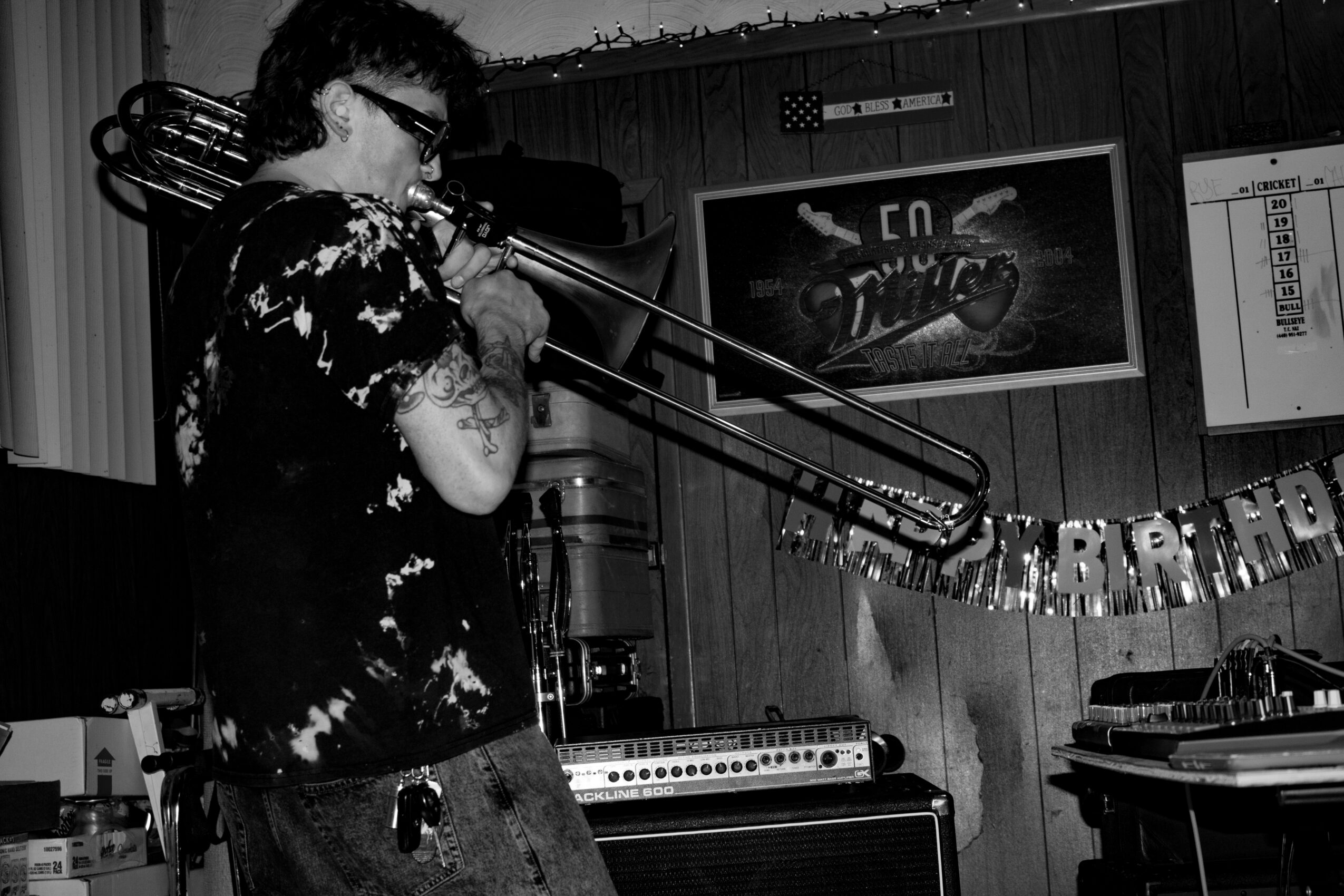 Person playing trombone in a room with musical equipment and a framed picture on the wall.