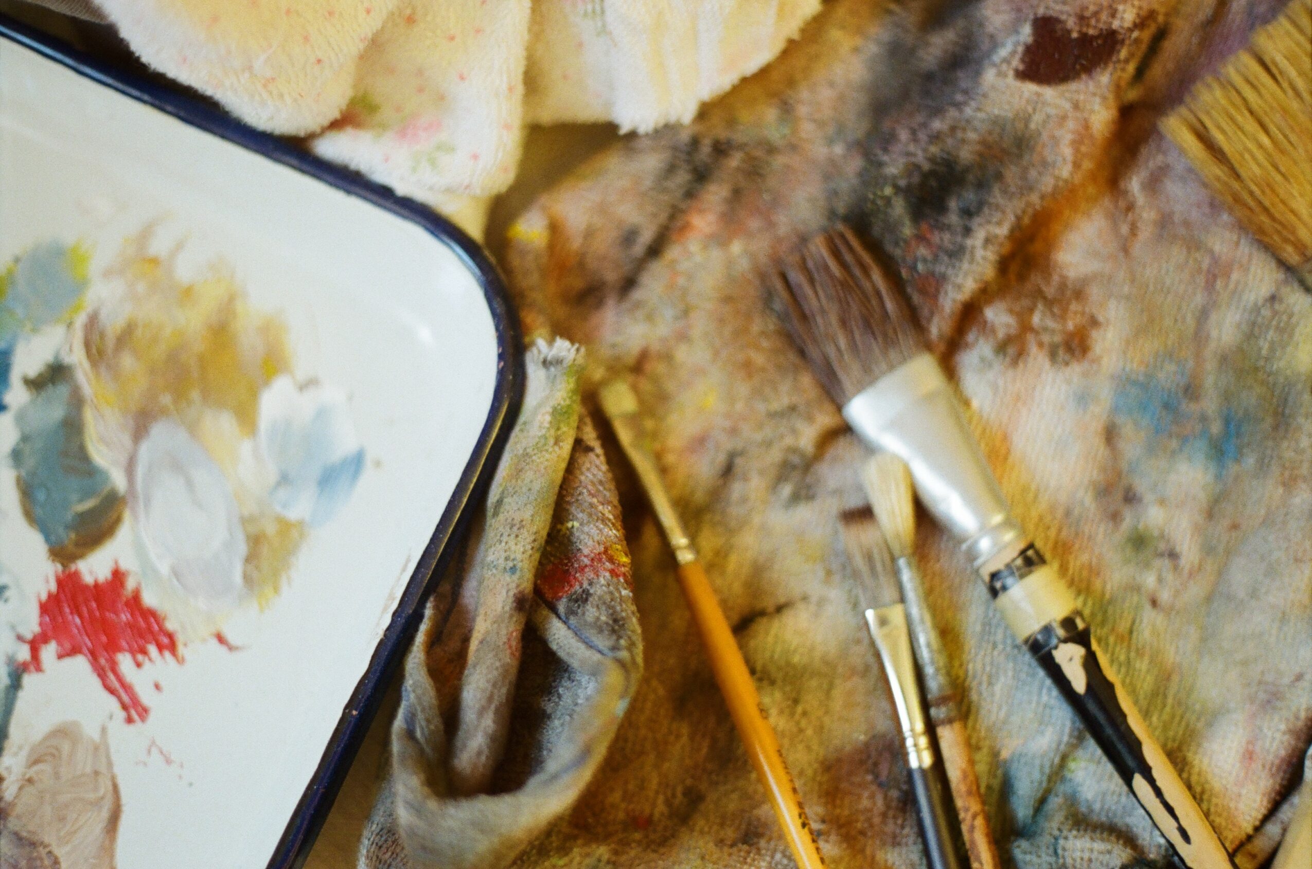 Paintbrushes, a palette, and sponge pieces on a paint-stained surface, with a partially visible palette and sponge pieces in the background.