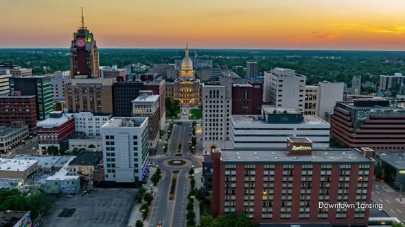 City skyline at sunset with prominent government building and surrounding structures, streets, and a sunset sky.