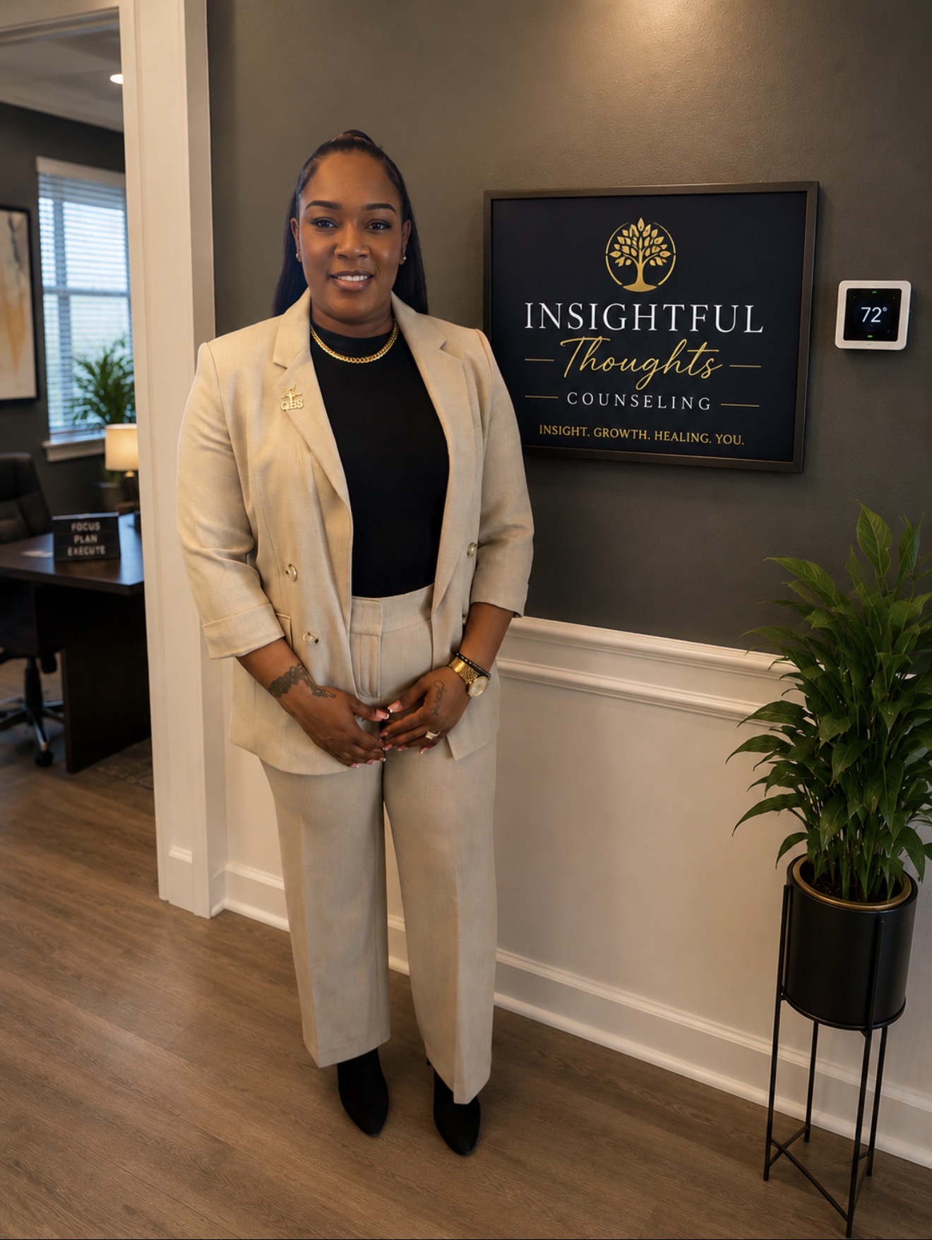 Woman in beige suit standing indoors with a sign reading 'Insightful Thoughts Counseling' behind her, next to a potted plant.