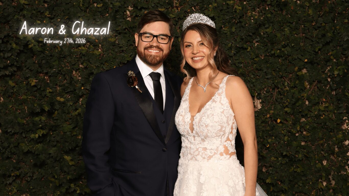 A smiling couple in formal attire stands in front of a green hedge, with text indicating their names and wedding date.