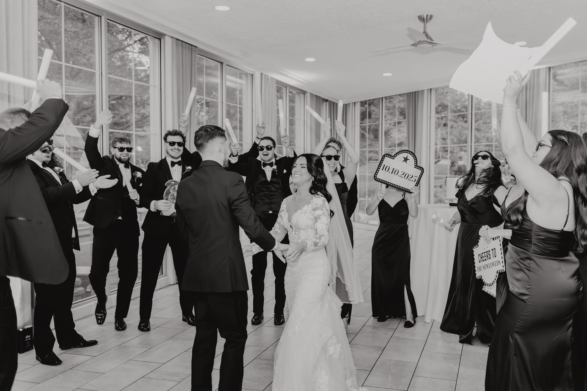 Group of people in formal attire celebrating indoors, some holding signs, with a bride and groom in the center.