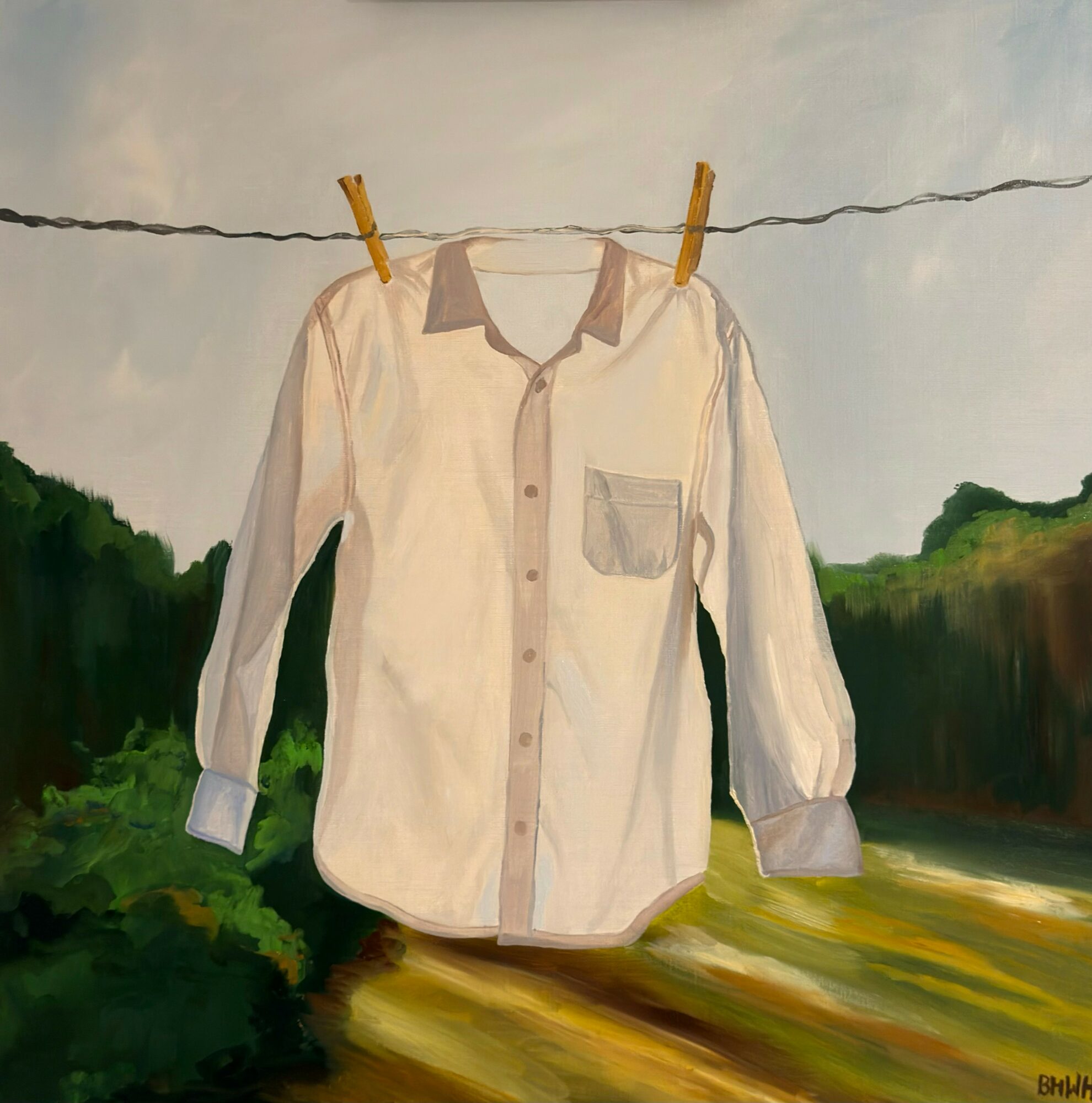 White long-sleeve shirt hanging on a clothesline with clothespins, outdoors with trees and a river in the background.