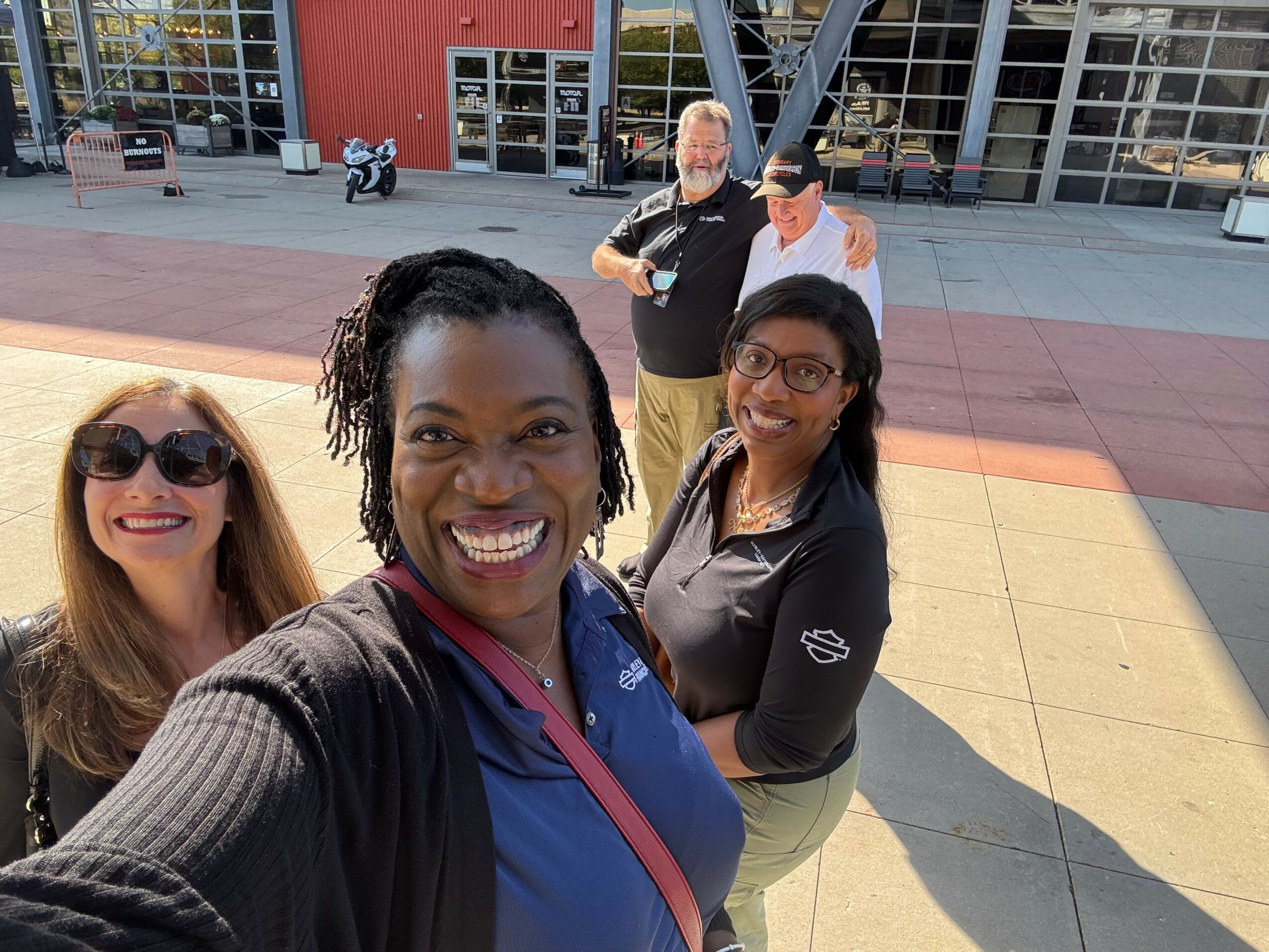 Four people smiling and posing for a photo outdoors, with a building and sidewalk in the background.