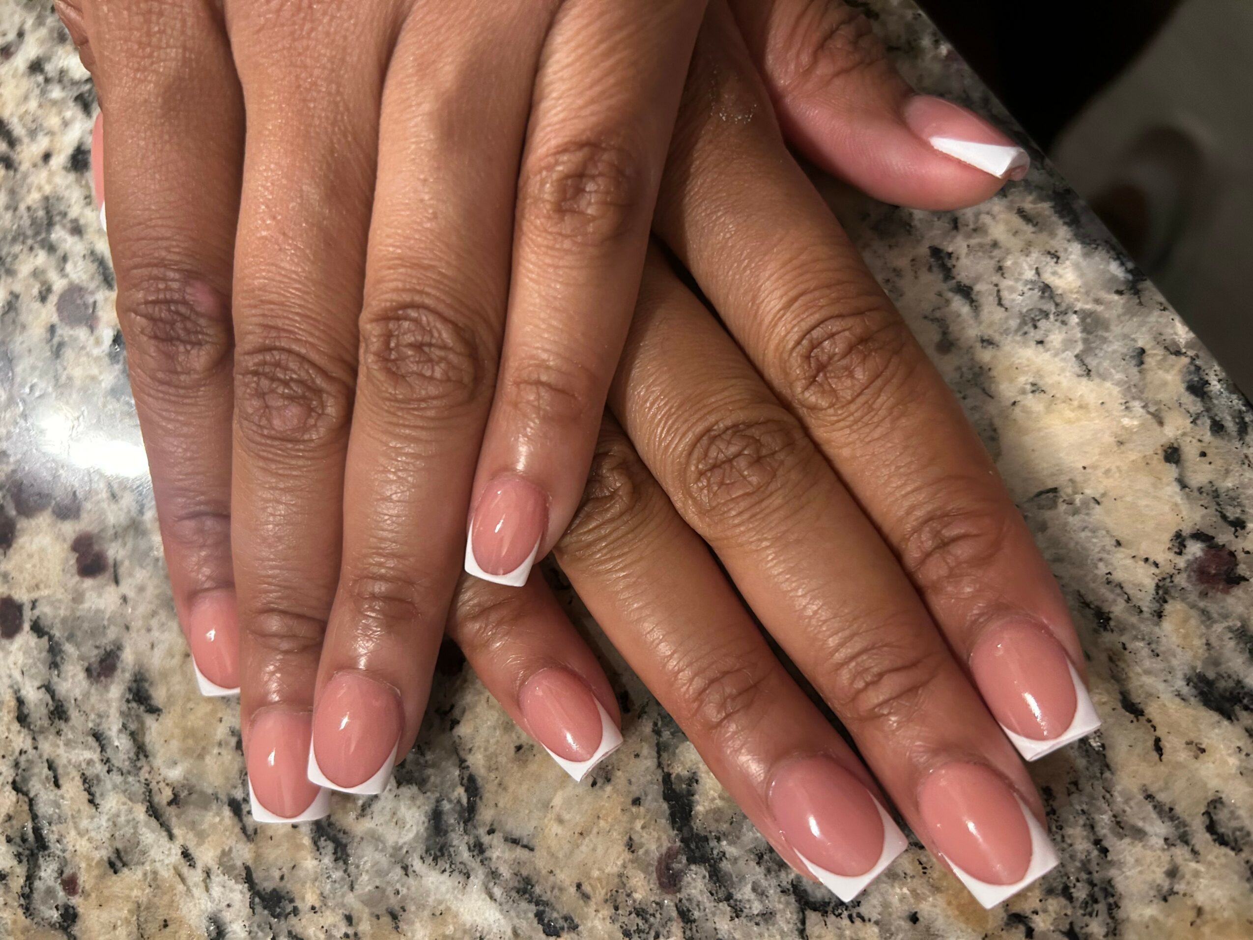 Two hands with manicured nails resting on a granite surface, showing well-groomed fingers and nails.