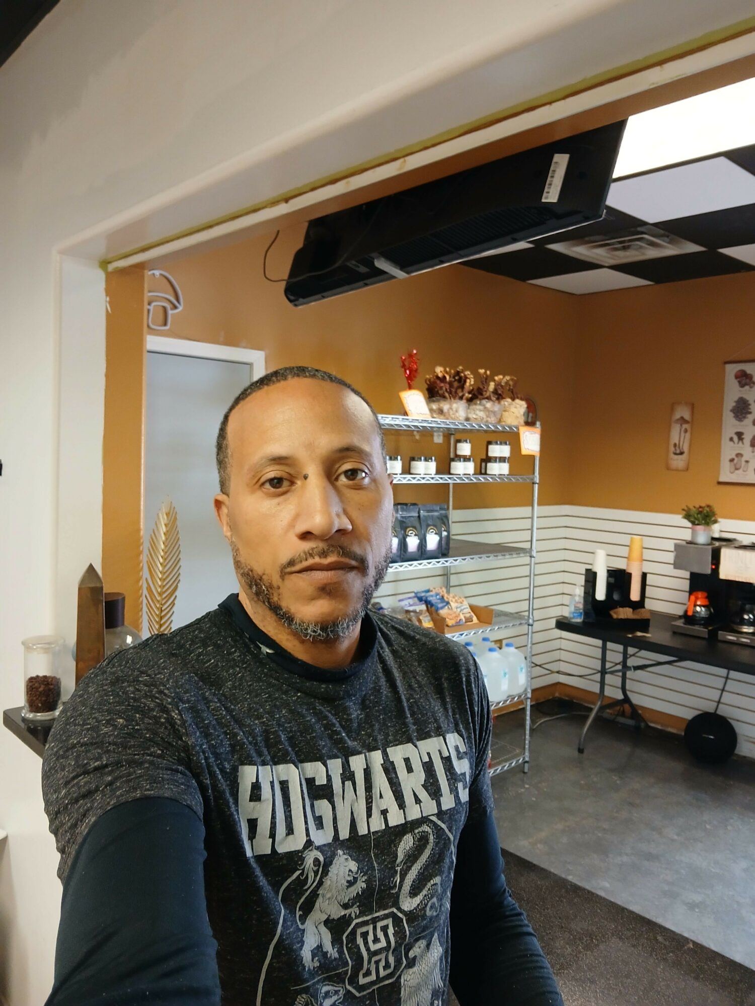 Person taking selfie in a cafe with display case and menu in background.