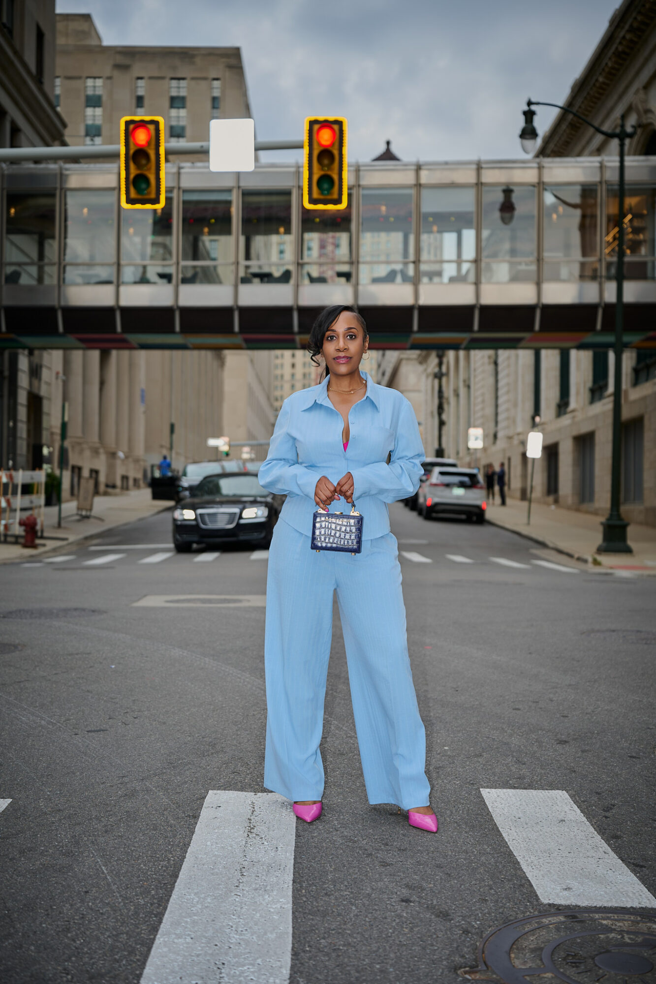 Woman in blue jumpsuit standing on crosswalk in city street with traffic lights overhead.