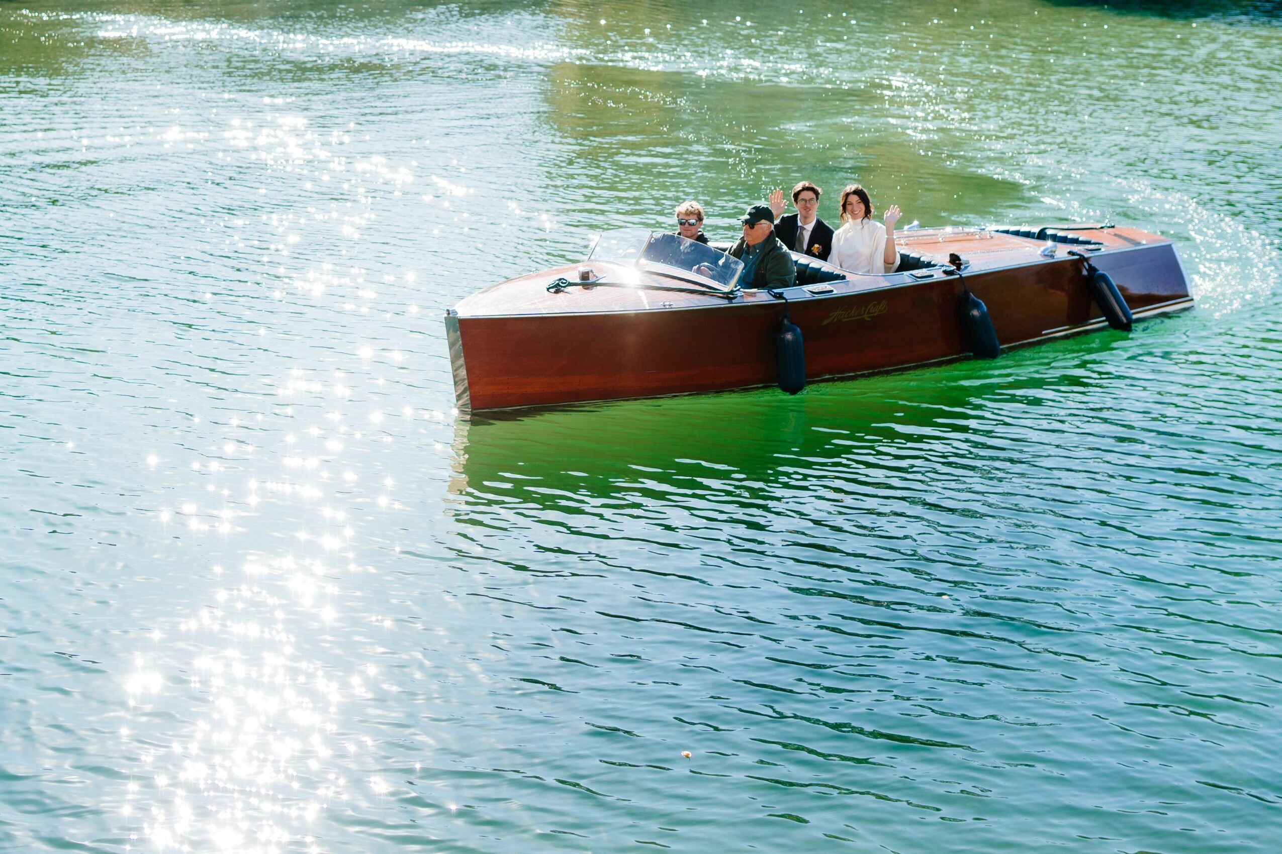 Four people are on a boat in green water, with sunlight reflecting on the surface.