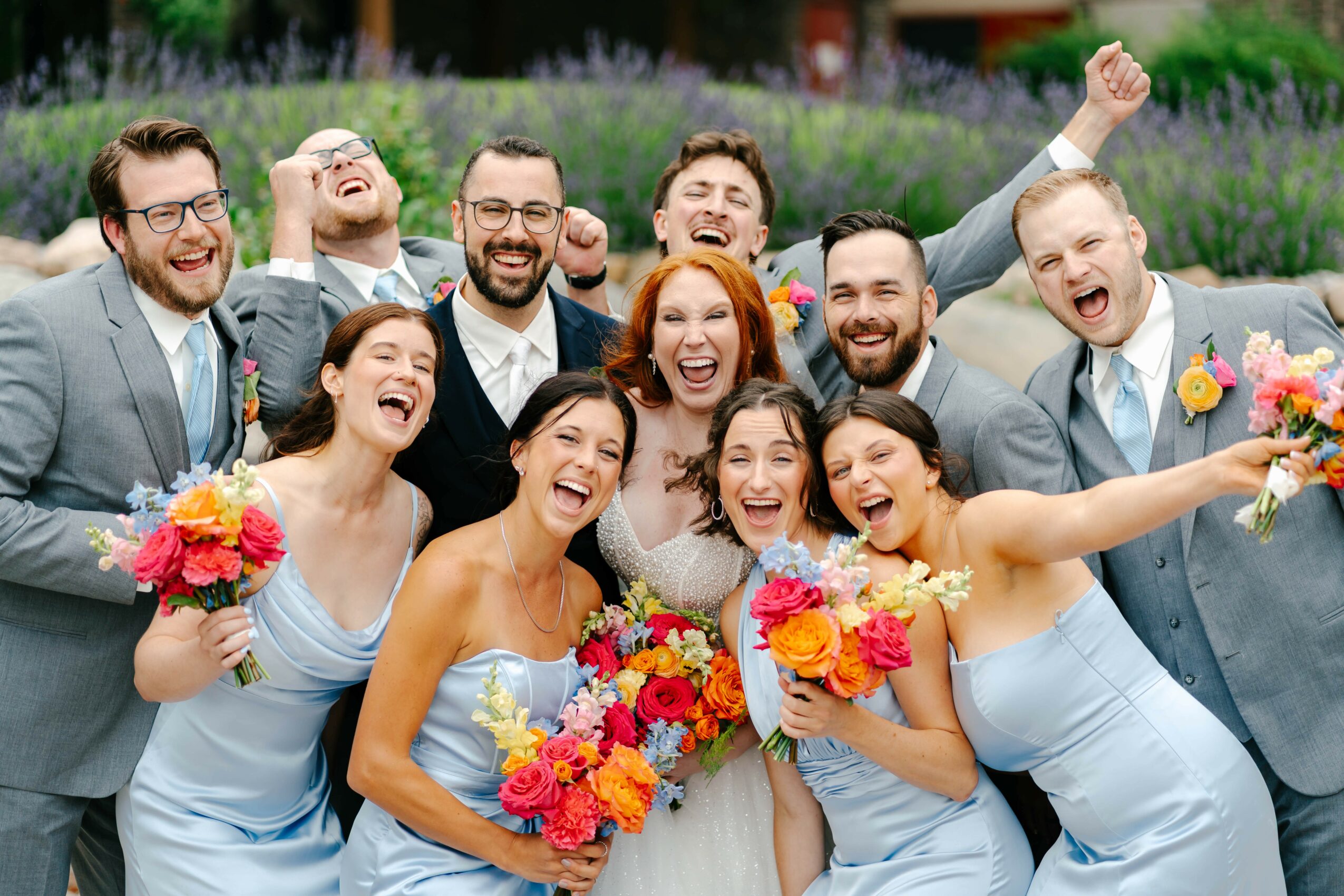 Group of smiling people in formal attire holding colorful bouquets outdoors, celebrating together.