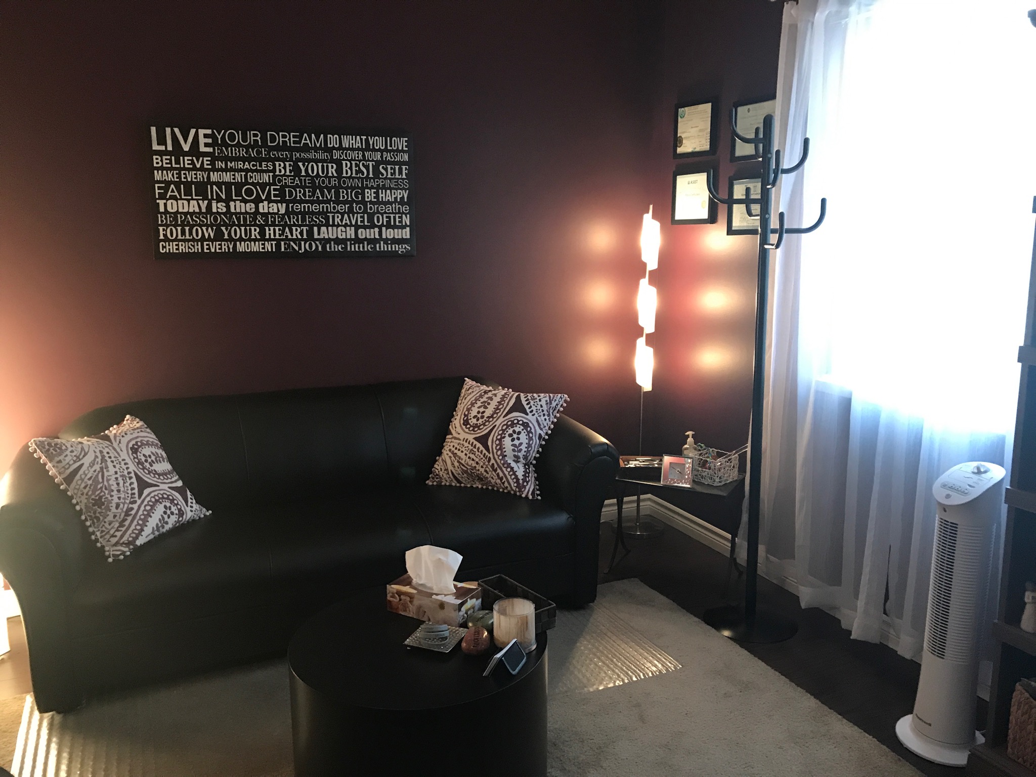 Living room with black sofa, patterned pillows, wall art, coat rack, and a window with curtains.