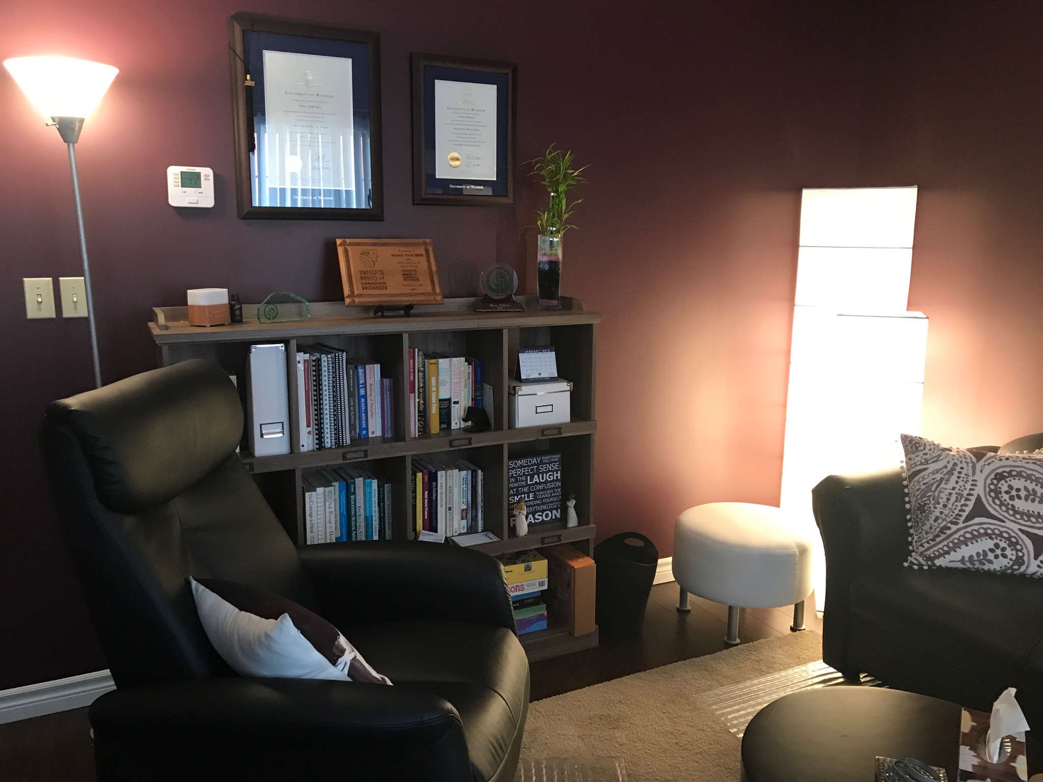 Living room corner with a black armchair, bookshelf, tall white lamp, and wall decorations.