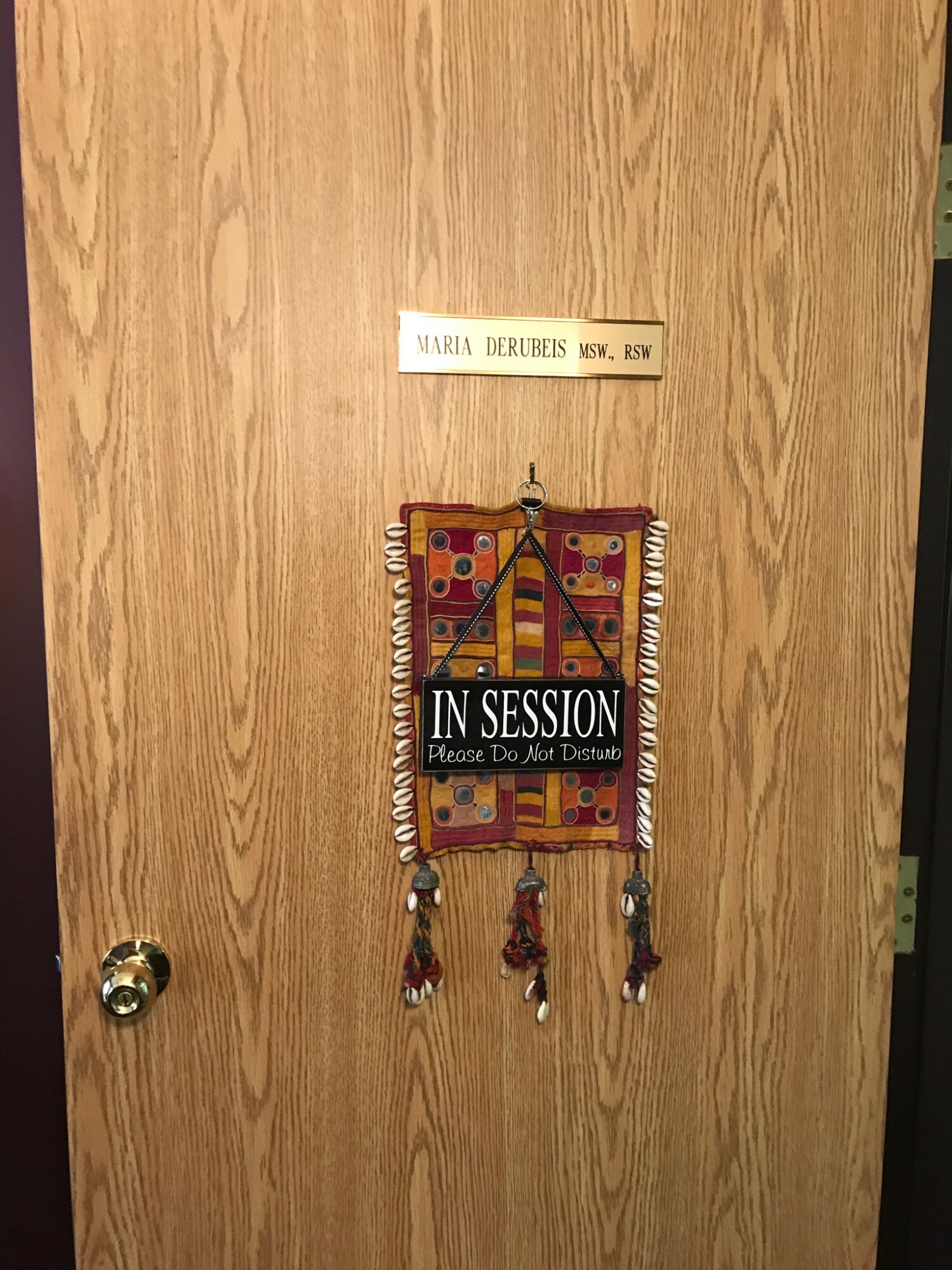 Wooden door with a decorative hanging and a sign above it, reading 'YARIS DERUBIES' and 'IN SESSION' below.