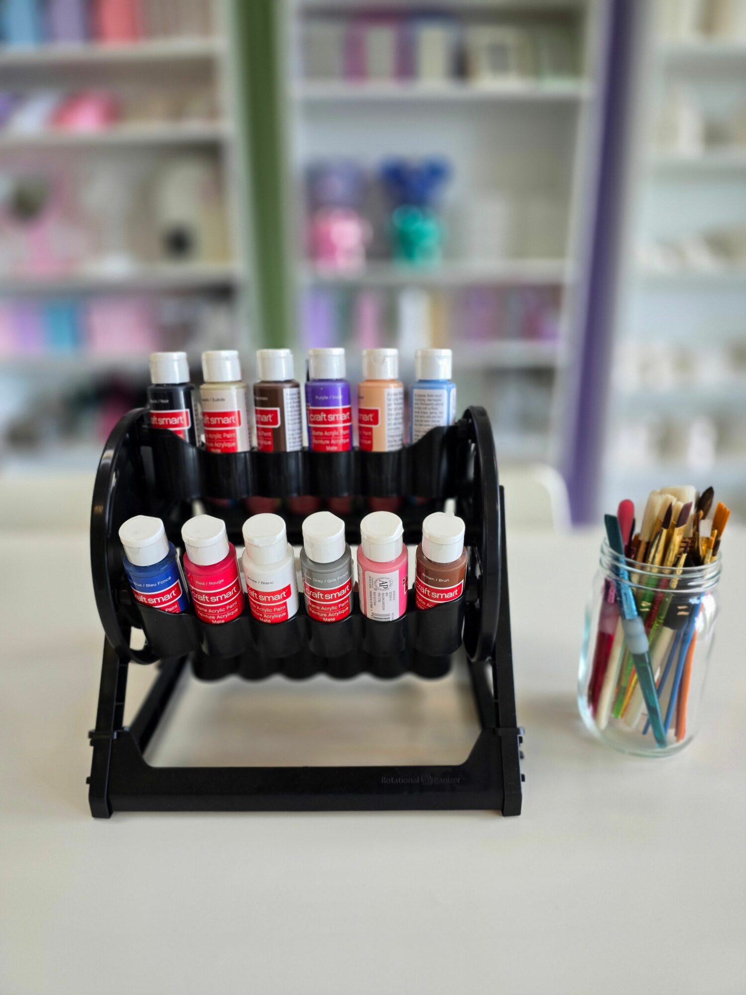 Black wall-mounted holder with white and red-capped bottles, a glass container with colored wires above, and blurred background.