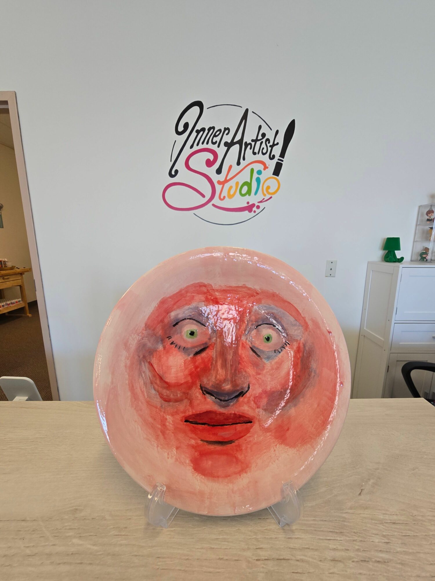 A pink balloon with a painted face, including eyes, nose, and mouth, placed on a wooden surface in a room.