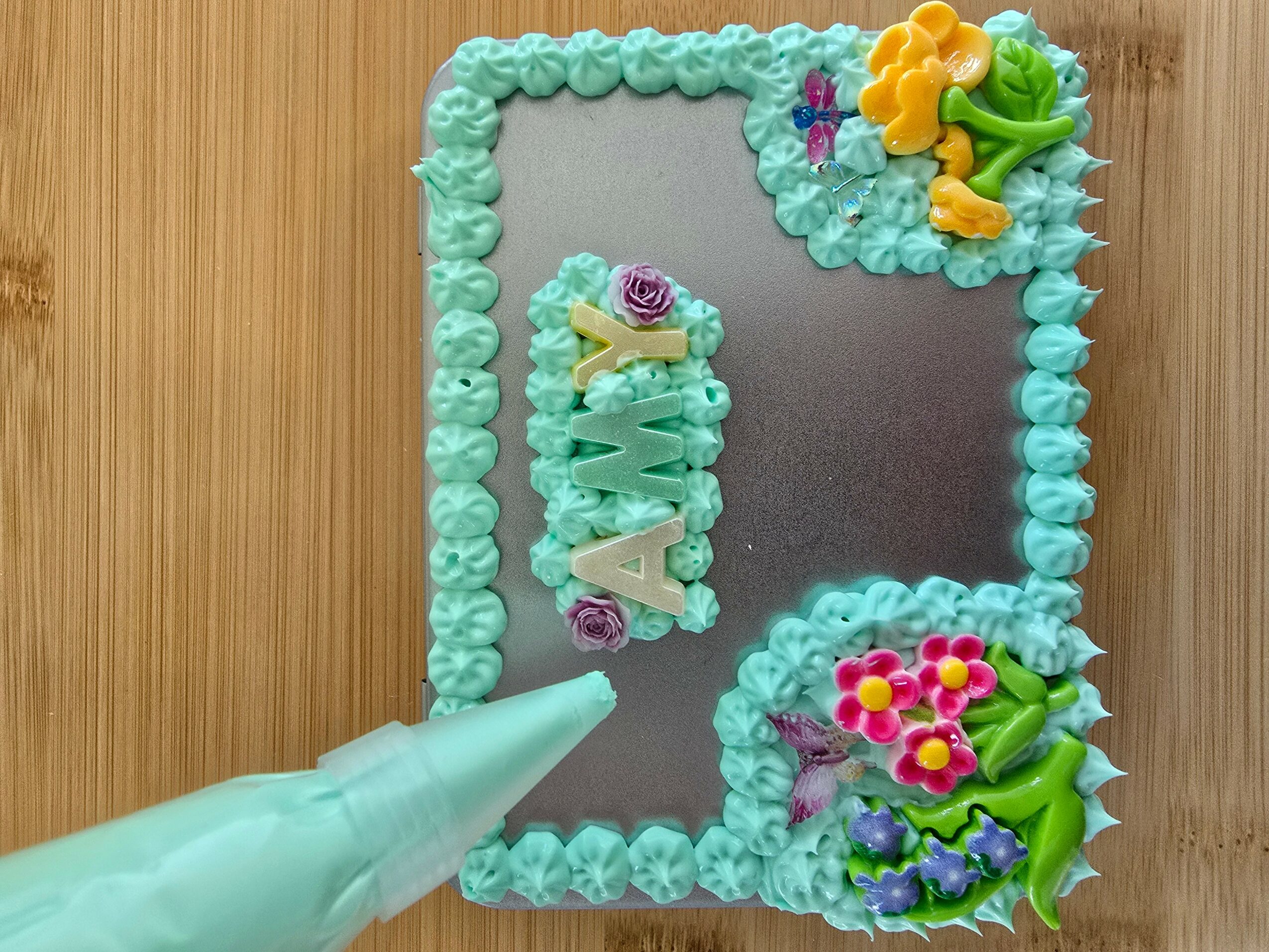 Decorative mirror with colorful flowers and a name spelled out in flowers, surrounded by a blue border, on a wooden surface.