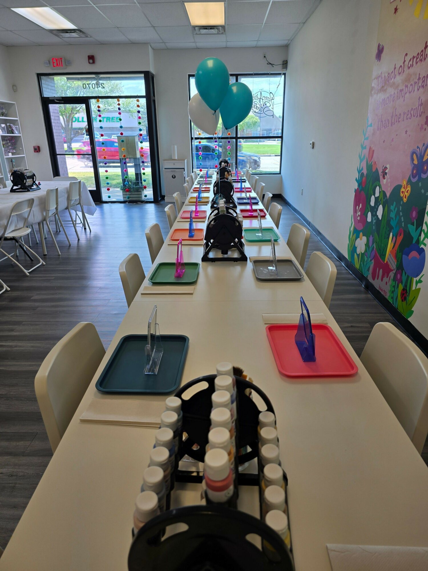 Long table with drinks, snacks, and a water bottle, in a room with large windows and colorful wall art.
