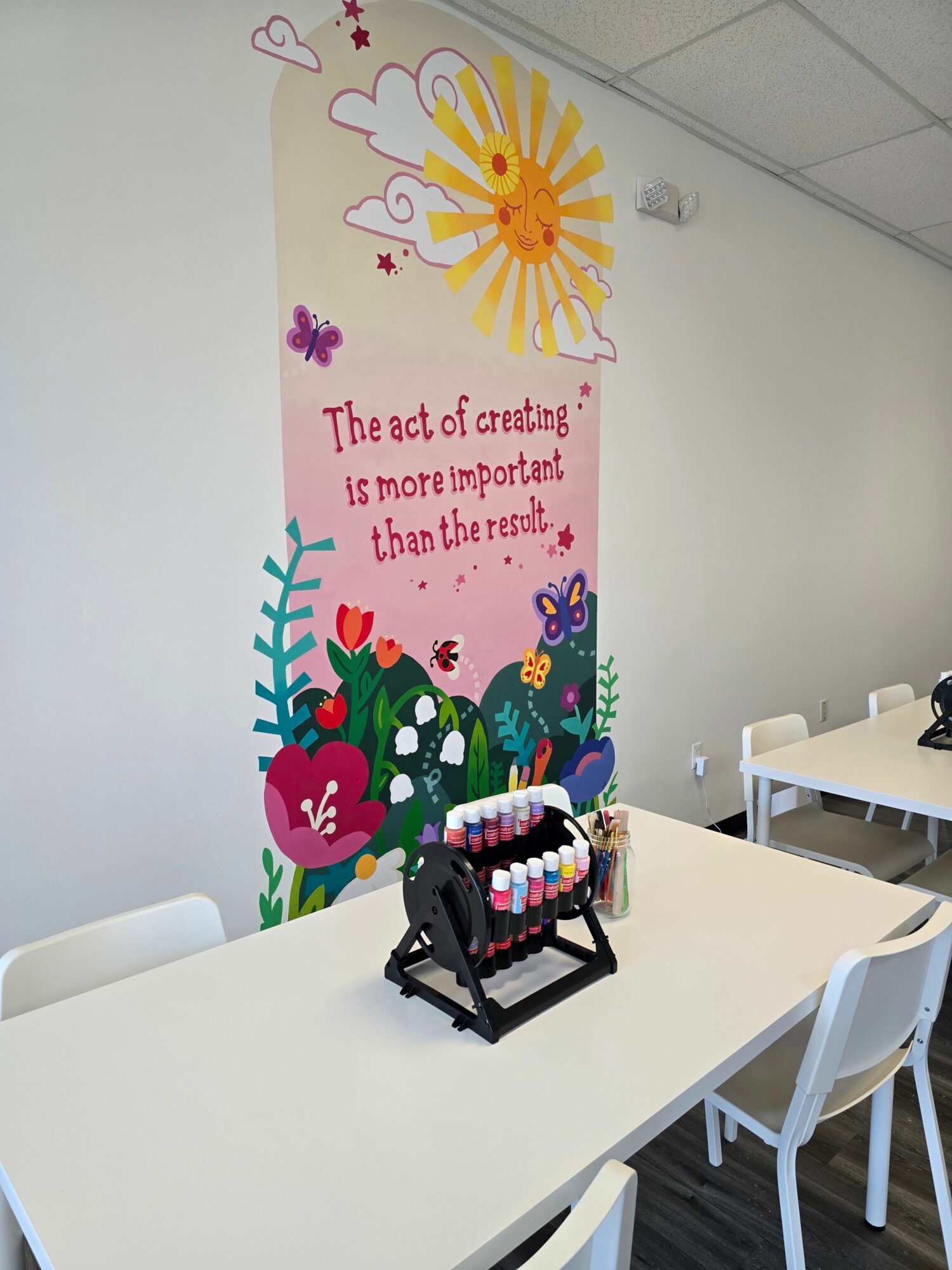 Colorful birthday banner with a sun, clouds, and flowers, and a table with a small black basket of candies on a white wall.