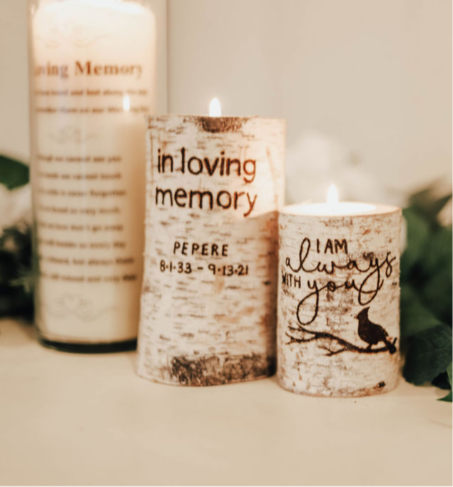 Three candles with engraved messages and a bird silhouette, placed on a light surface with blurred background.