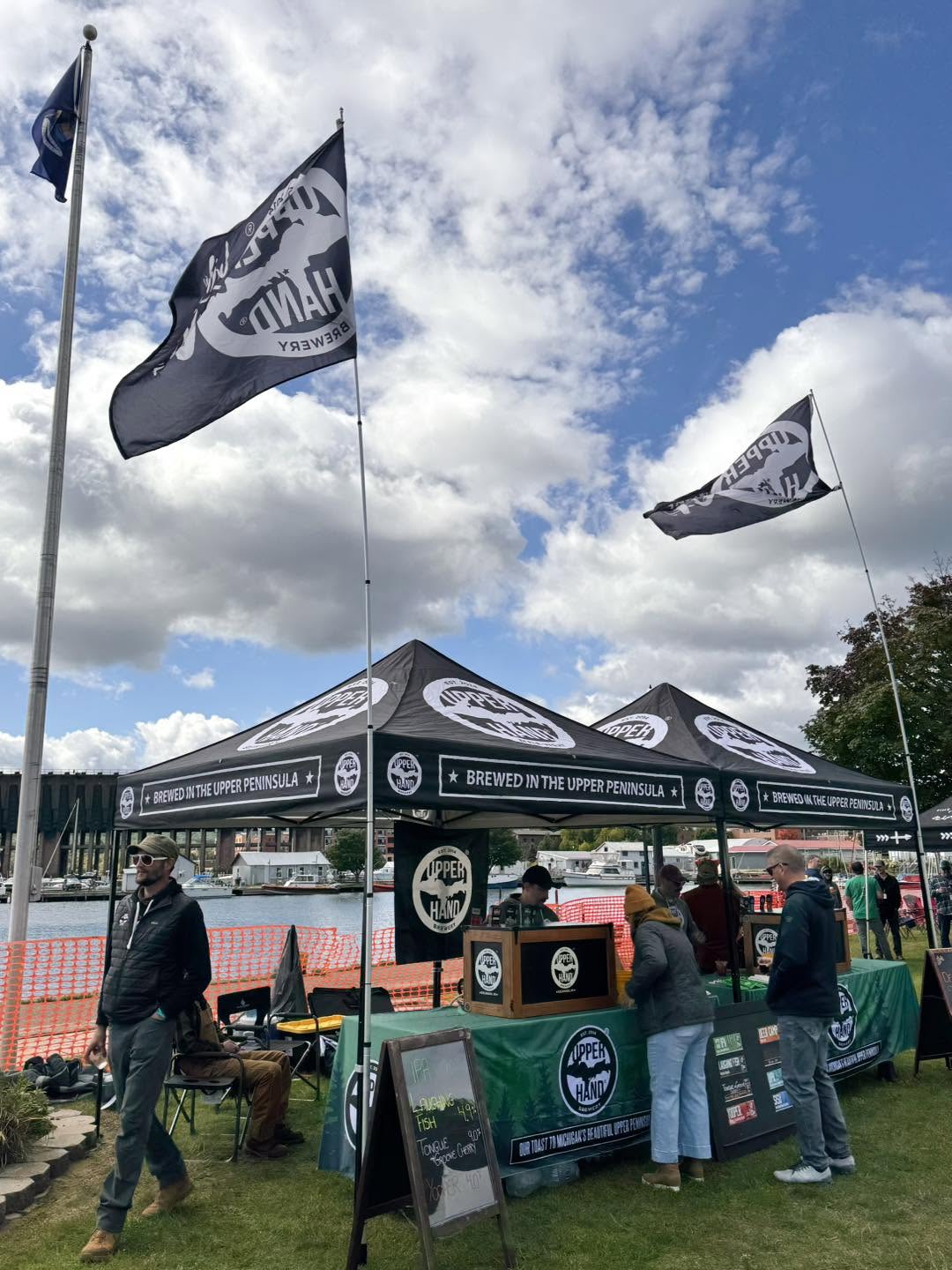 Outdoor event with tents, flags, and people under a partly cloudy sky.