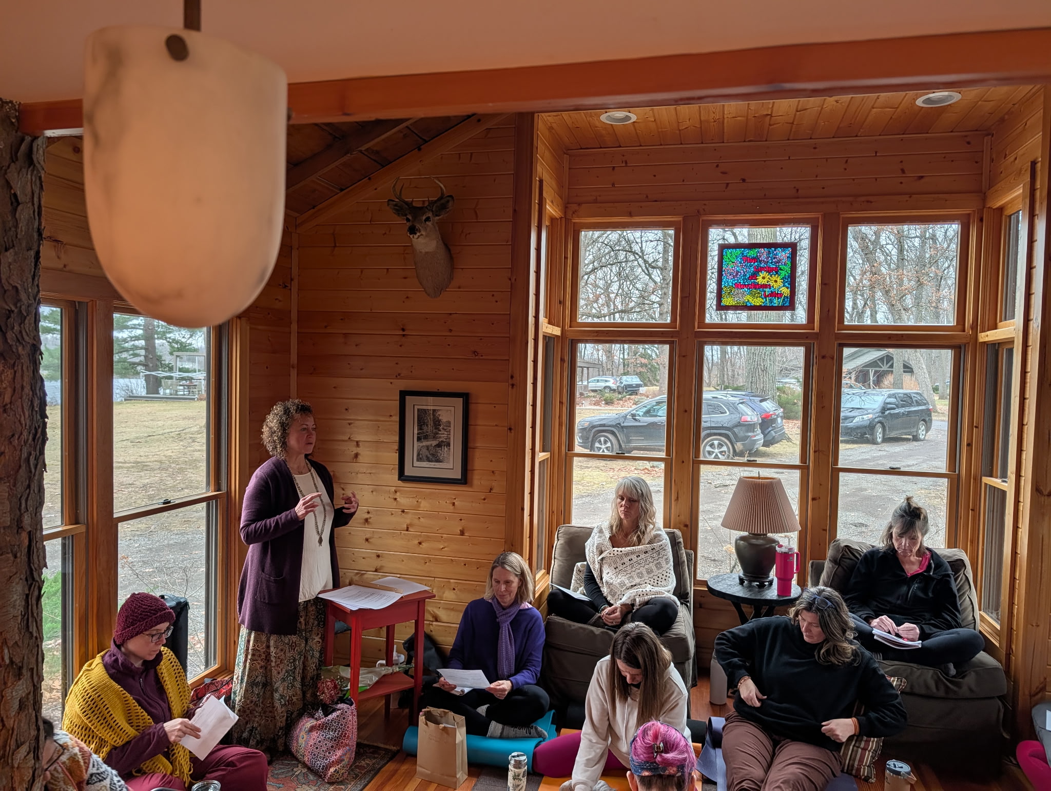 Group of people sitting and reading in a wooden room with large windows and natural light.