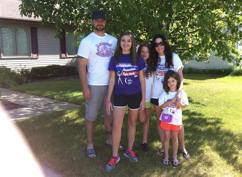 Group of five people standing outdoors under a tree, smiling, with a house in the background.