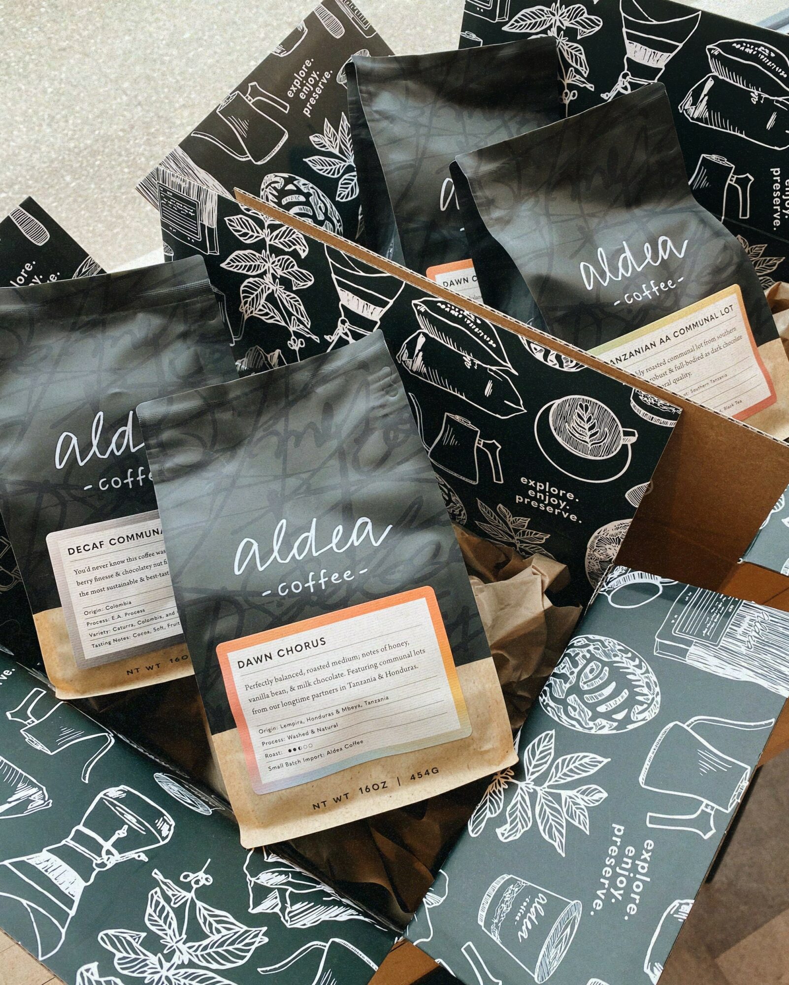 Several coffee bags and boxes with black and white packaging, some with illustrations of coffee beans and leaves, on a surface.