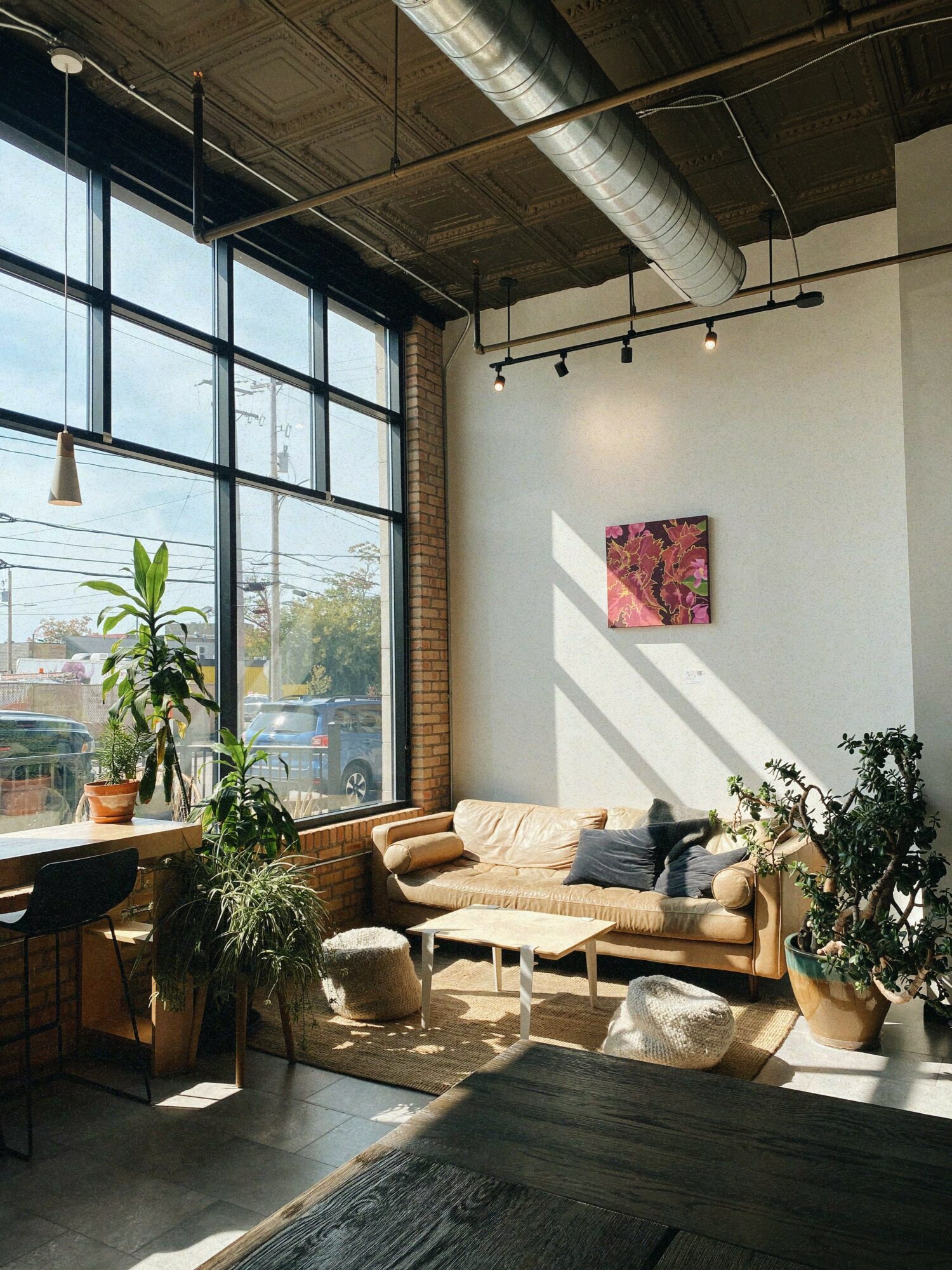Interior of a modern room with large windows, a beige sofa, plants, and a small painting on the wall.
