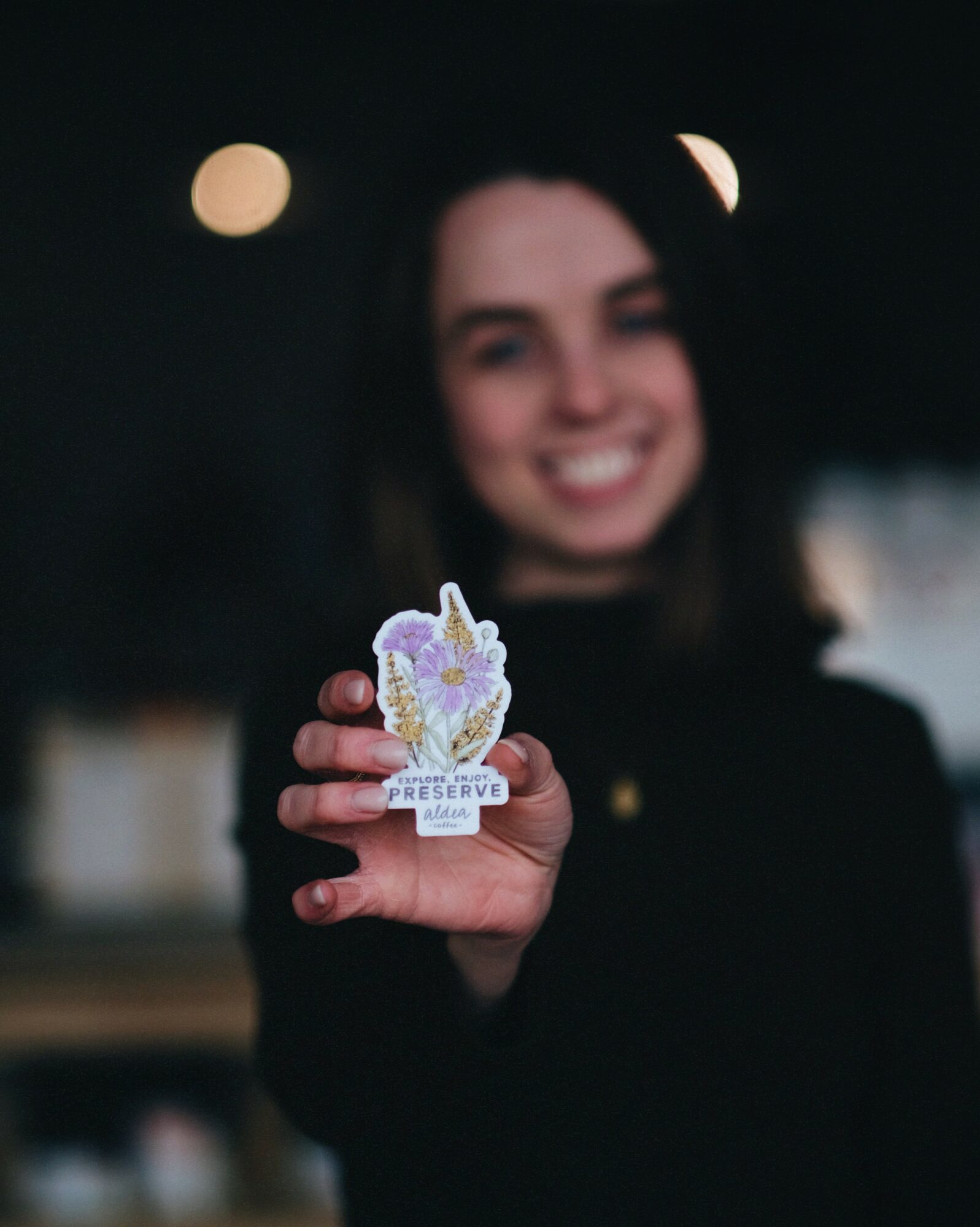 Person smiling and holding a small decorative object with a purple and white design, blurred background.
