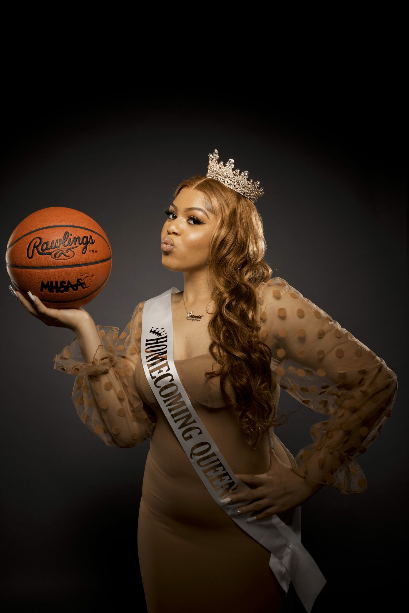 Woman wearing a crown and sash holding a basketball, dark background, long curly hair, elegant dress.