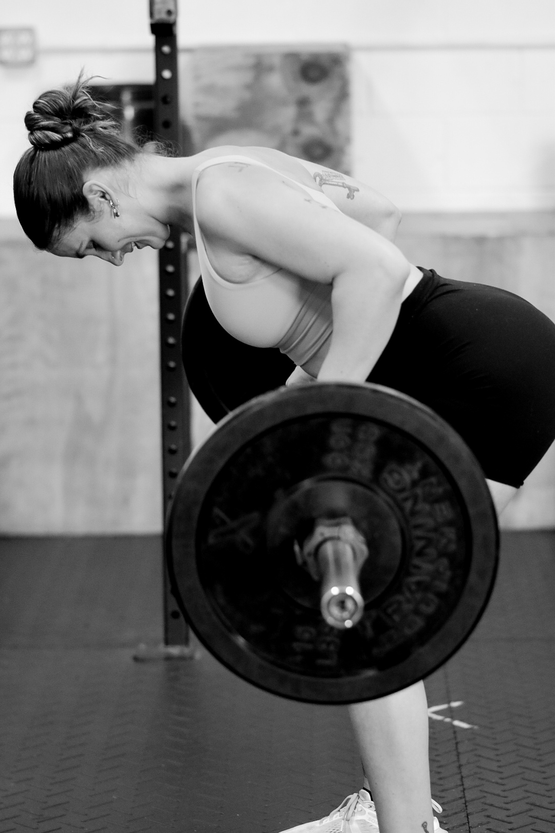 Woman lifting a barbell in a gym, bent forward with her back straight, wearing a sports bra and leggings.