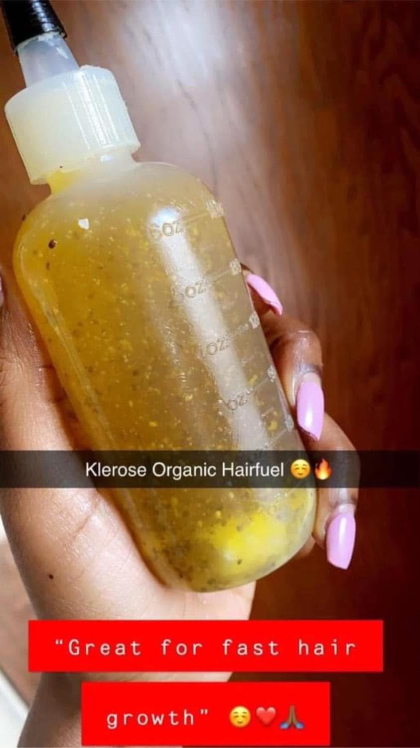 Hand holding a yellow bottle with a dropper cap, labeled 'Klerose Organic Hairfuel,' with a wooden surface background.