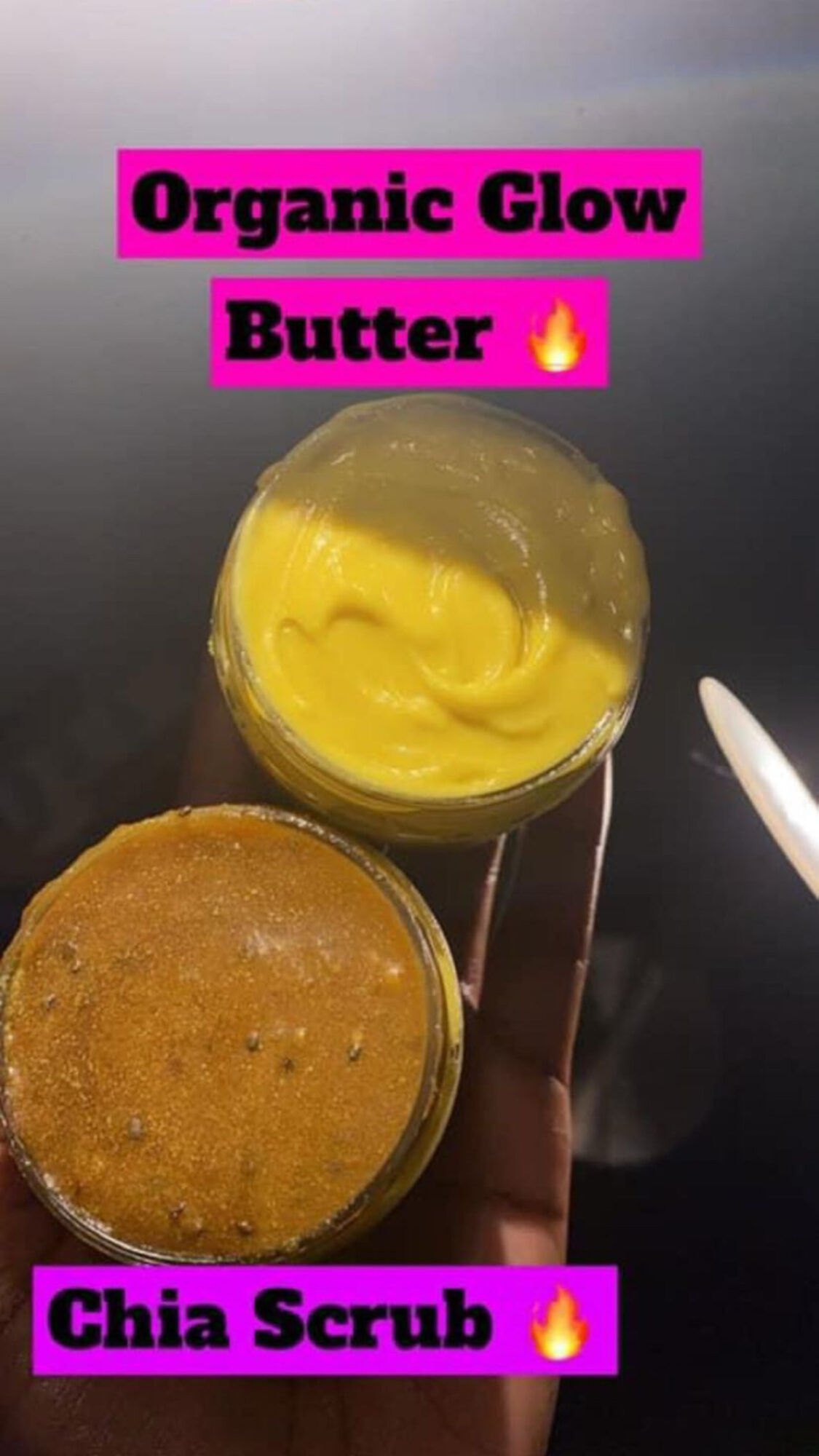 Hand holding two jars of skincare products, one with yellow butter and the other with chia scrub, against a dark background.